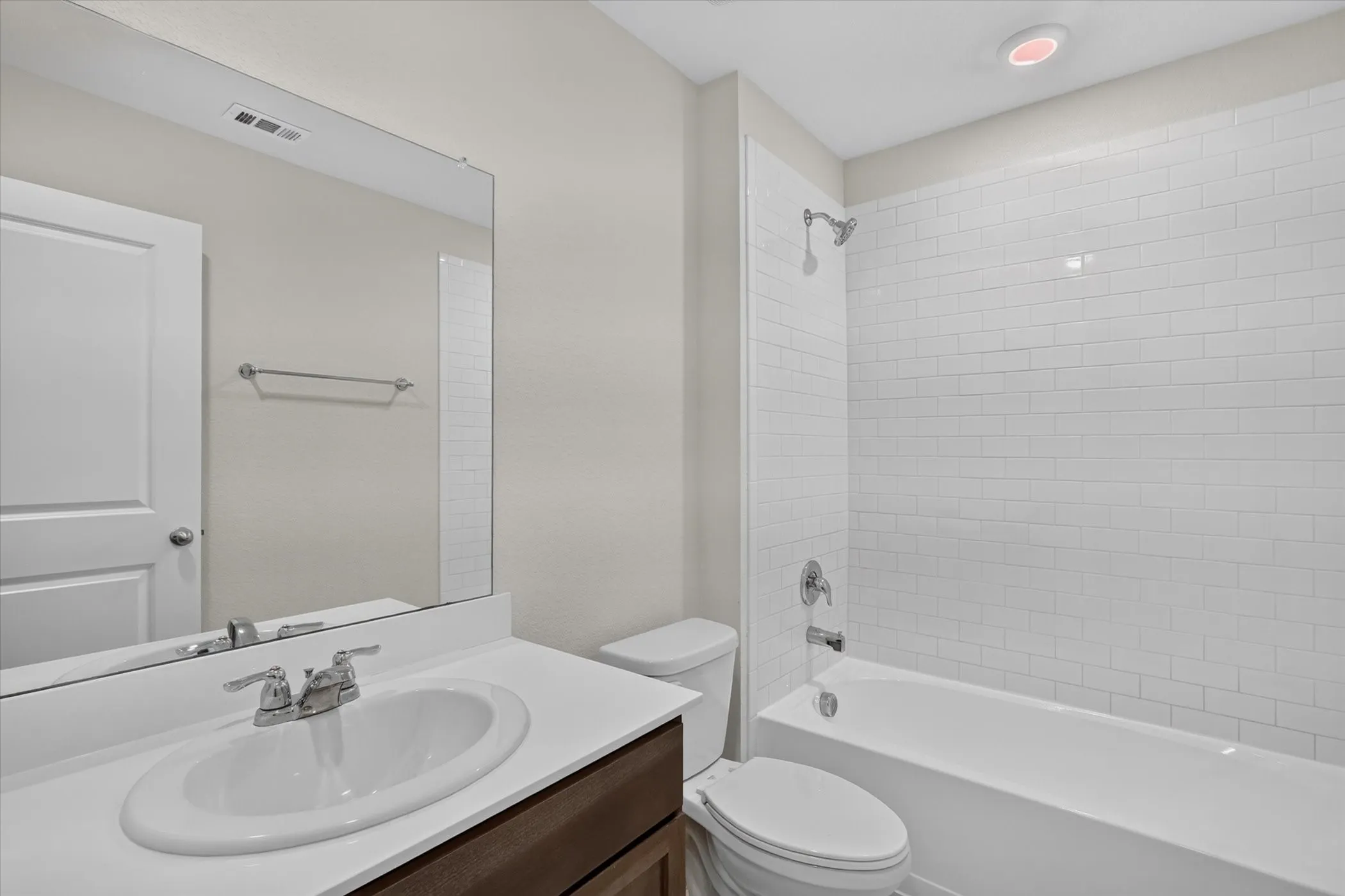 White subway tile shower surround, chrome shower fixtures, white bathtub, vanity with integrated sink, and stainless steel faucet