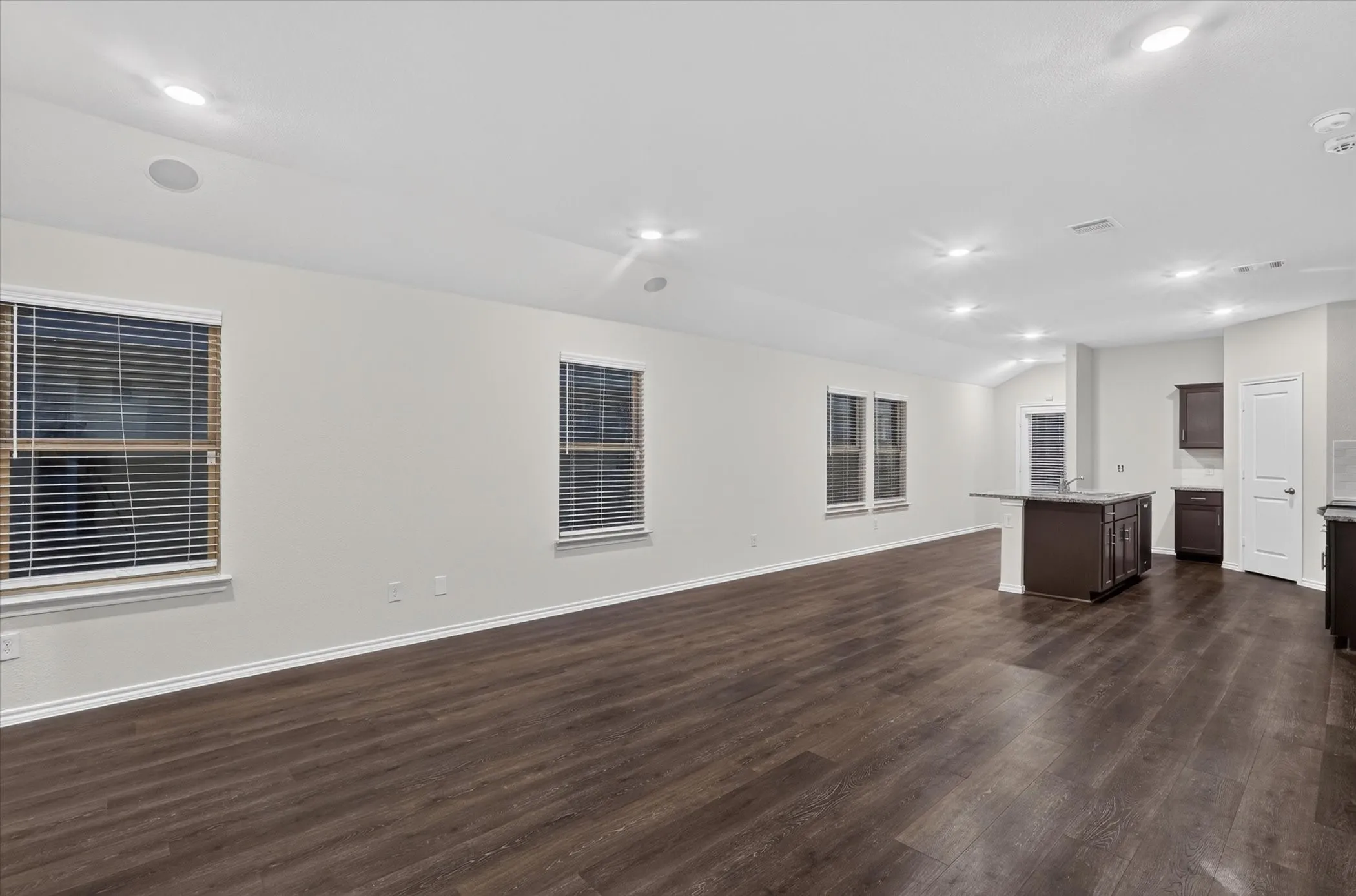Spacious open-concept interior featuring wood-finish flooring, recessed lighting, multiple windows with blinds, and a kitchen island with built-in cabinetry