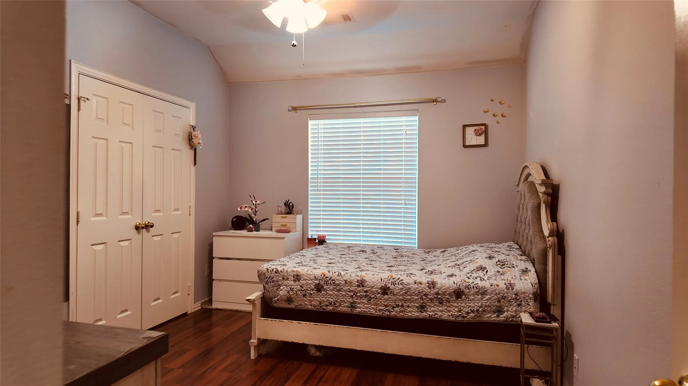 Wood-finish flooring, vaulted ceiling, window with blinds, ceiling fan with light, and bi-fold closet doors