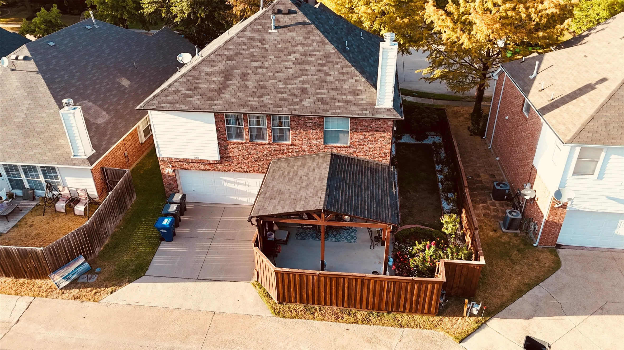 Two-story residence featuring a brick and siding exterior, an attached garage, and a covered outdoor patio with a wood-fenced enclosure