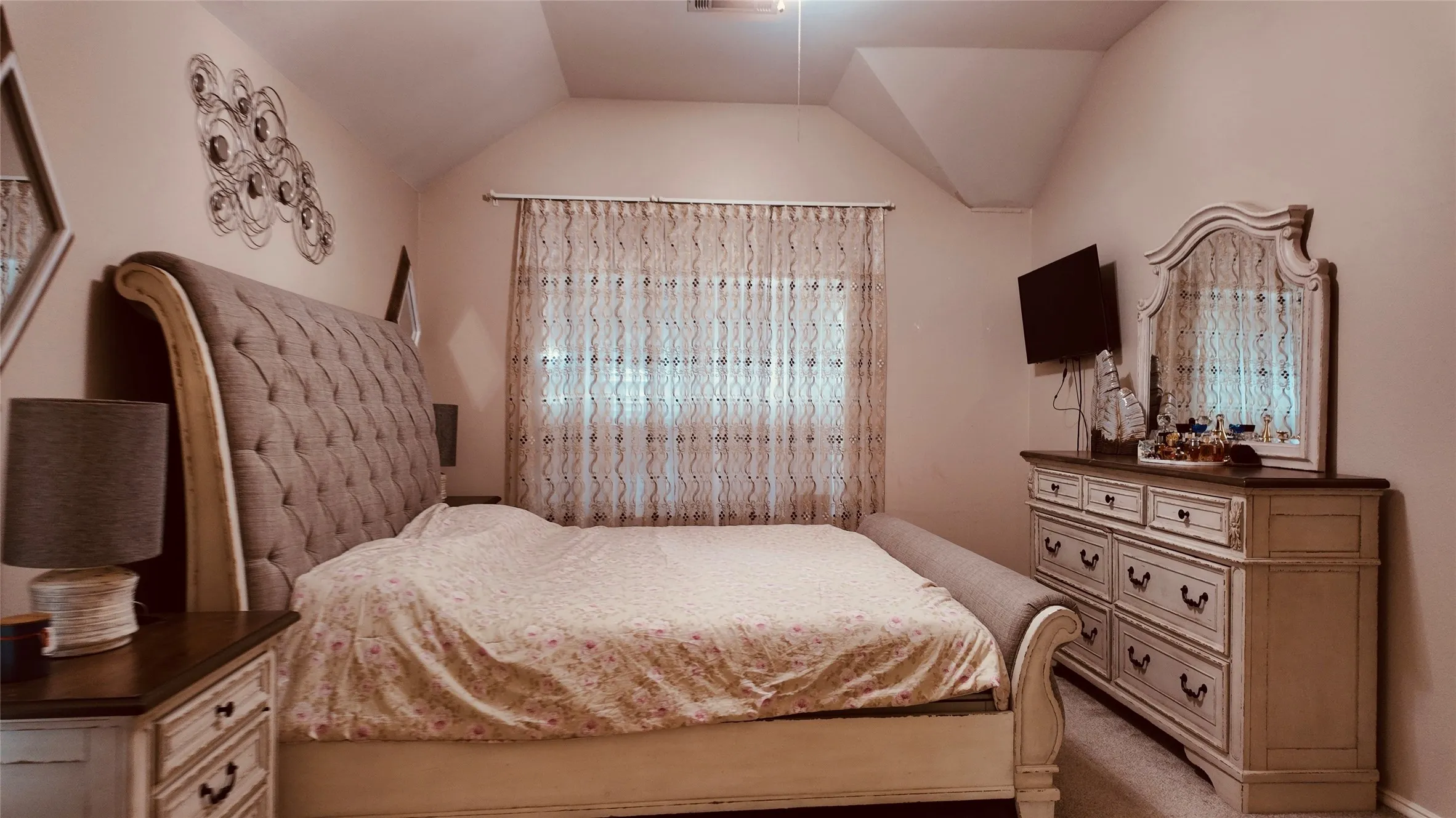 Vaulted ceiling design, wall-mounted television, and a window with sheer curtains