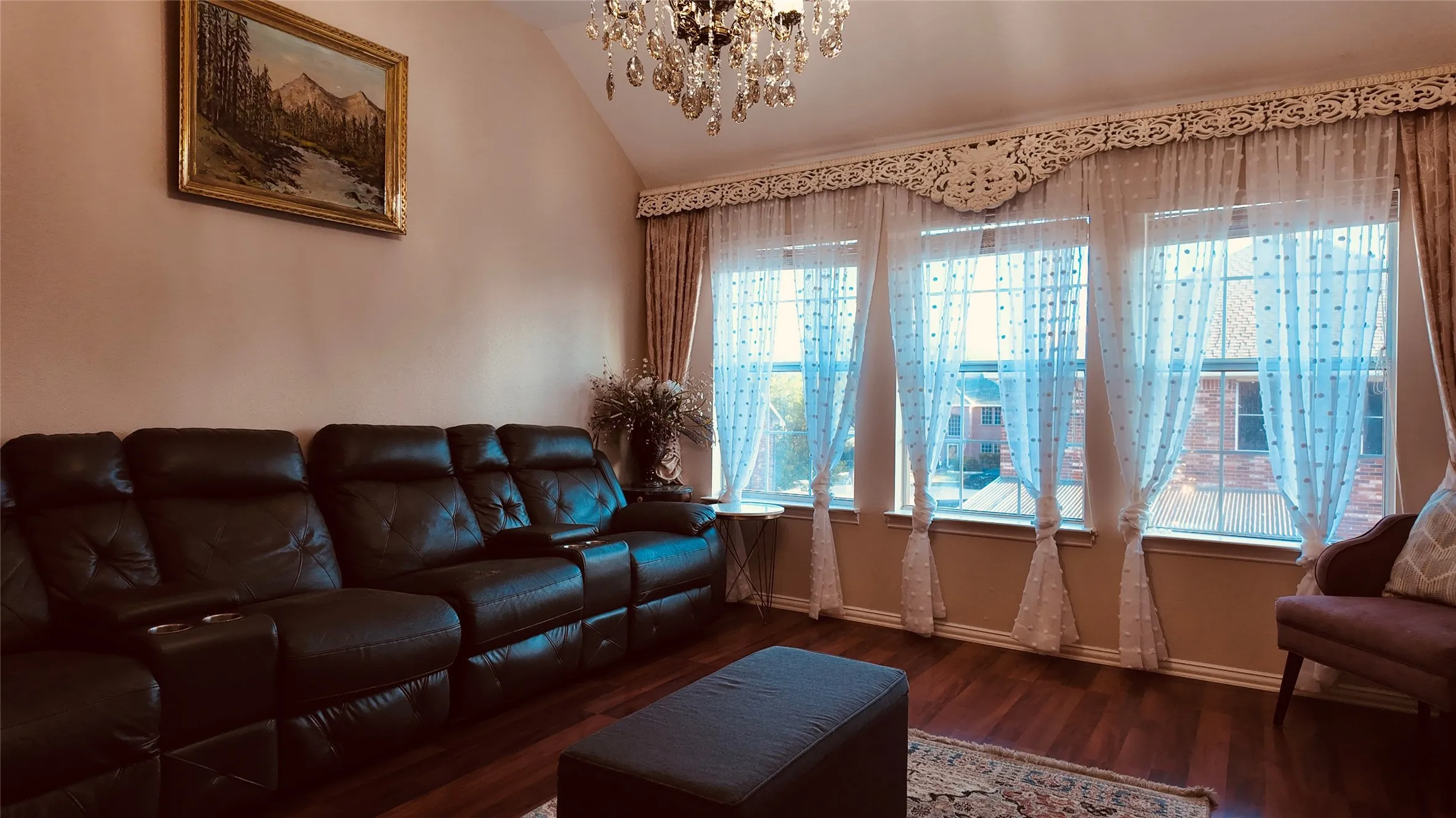 Vaulted ceiling with a crystal chandelier, multiple large windows, and dark wood-finish flooring