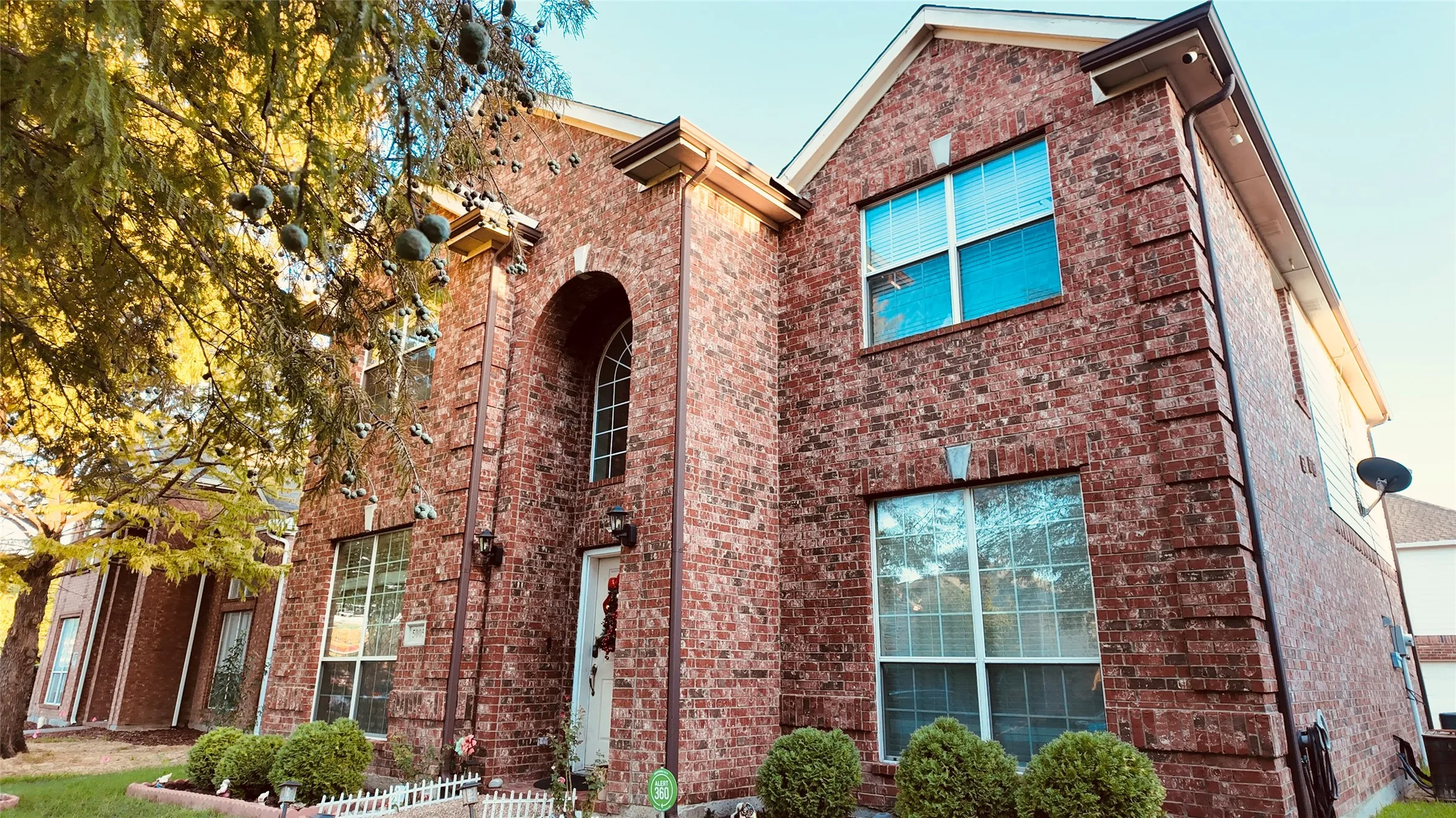 Two-story brick facade, arched entryway, white window frames, attached gutters, and a pitched roofline