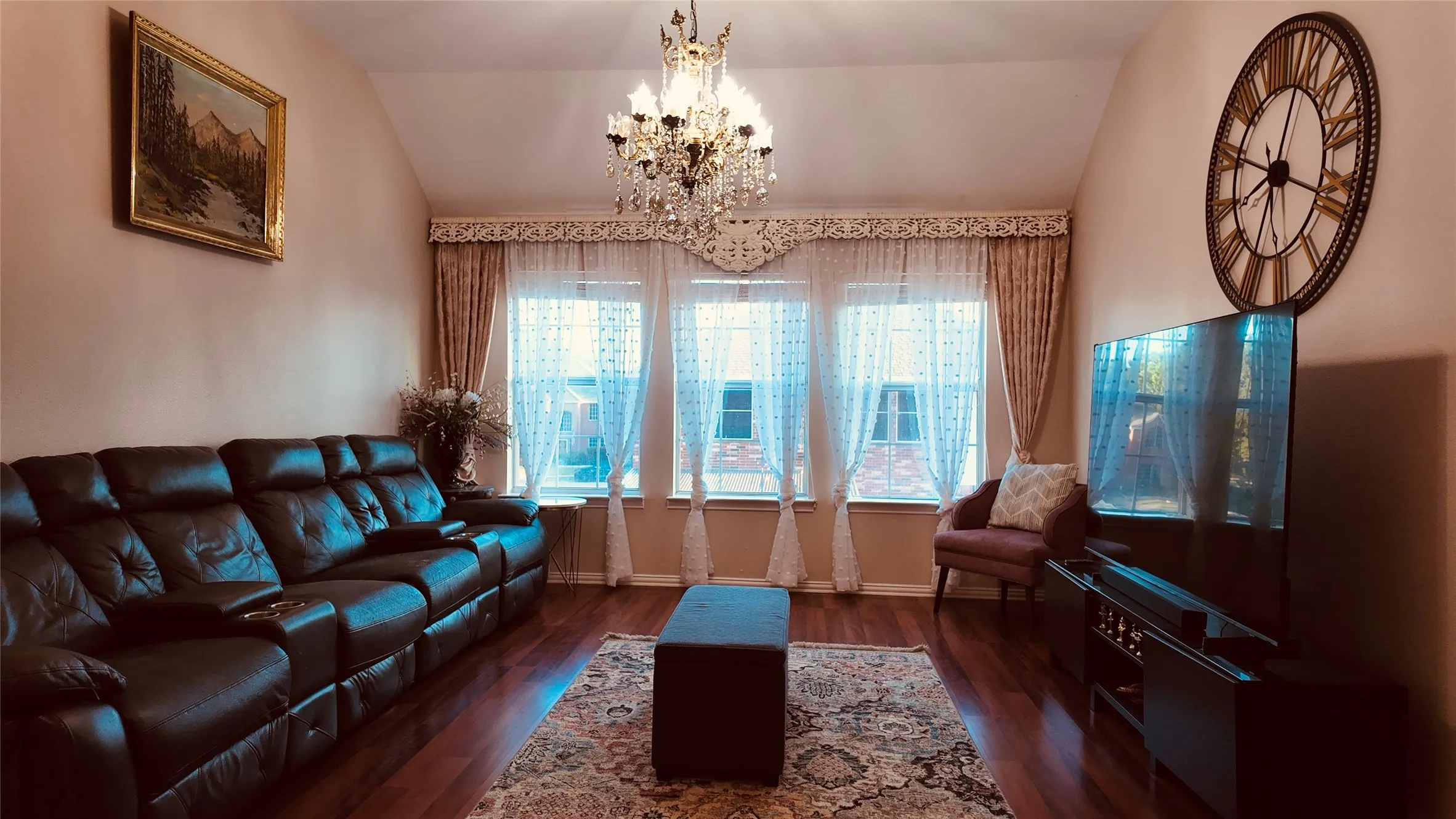 Vaulted ceiling with a crystal chandelier, wood-finish flooring, and a bank of three windows