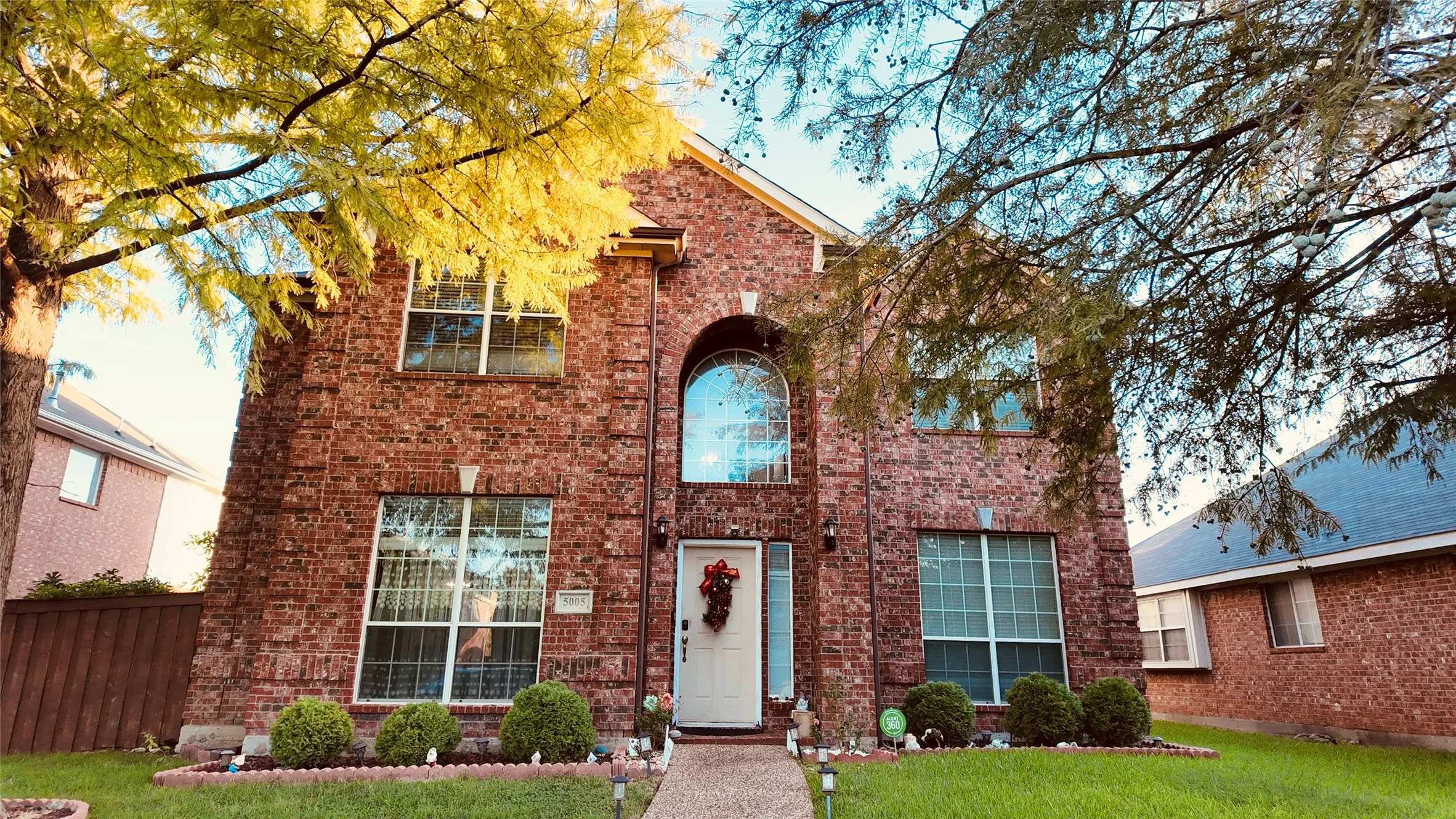 Brick exterior with arched window, white front door, established shrubbery, and a concrete pathway