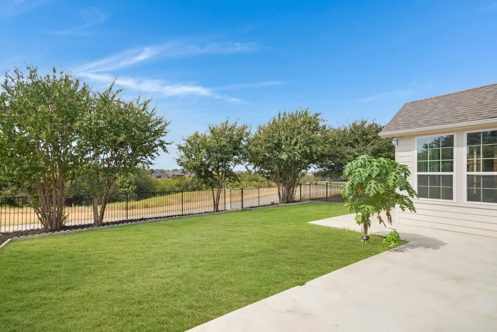 Expansive green lawn with a concrete patio, bordered by a black metal fence