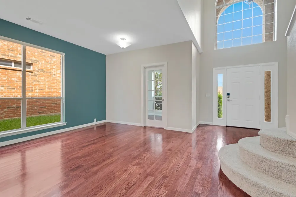 Hardwood-finish flooring throughout, complemented by a large picture window, a two-story arched window, and a white paneled entry door with sidelights