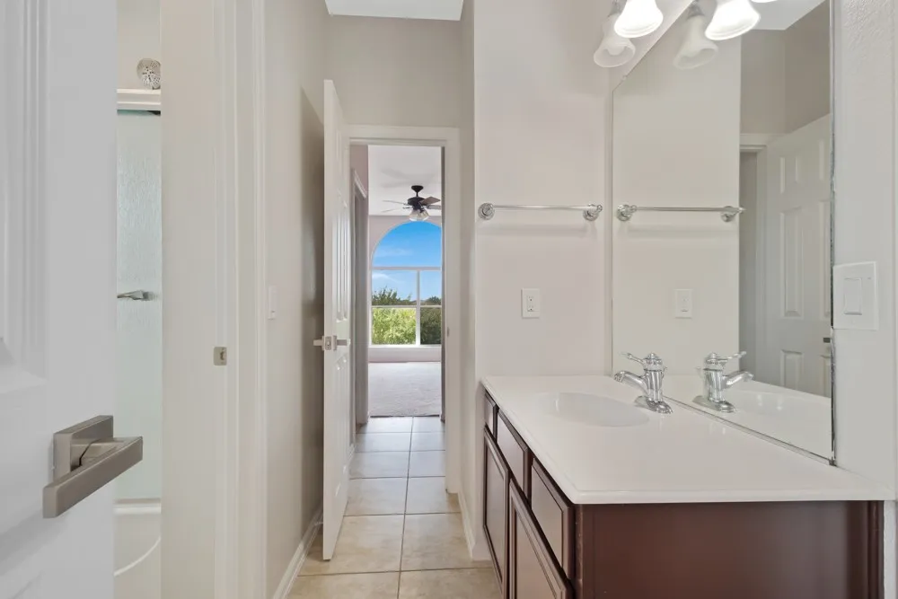 Vanity with an integrated sink and chrome faucet, large wall-mounted mirror, three-light fixture, and tile flooring