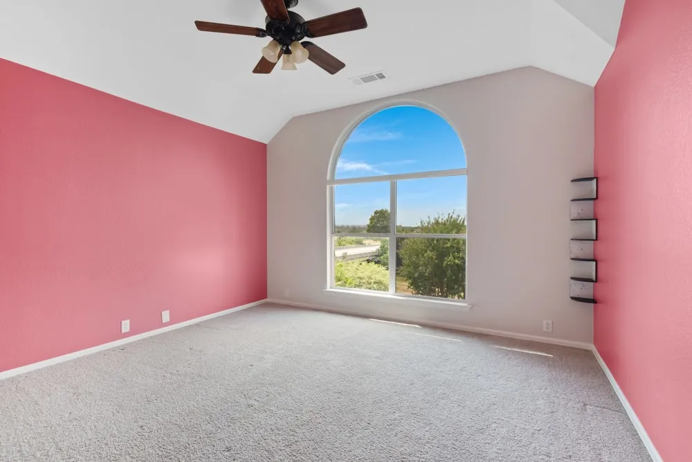 Arched window, vaulted ceiling, ceiling fan with light fixture, carpeted flooring, built-in shelving