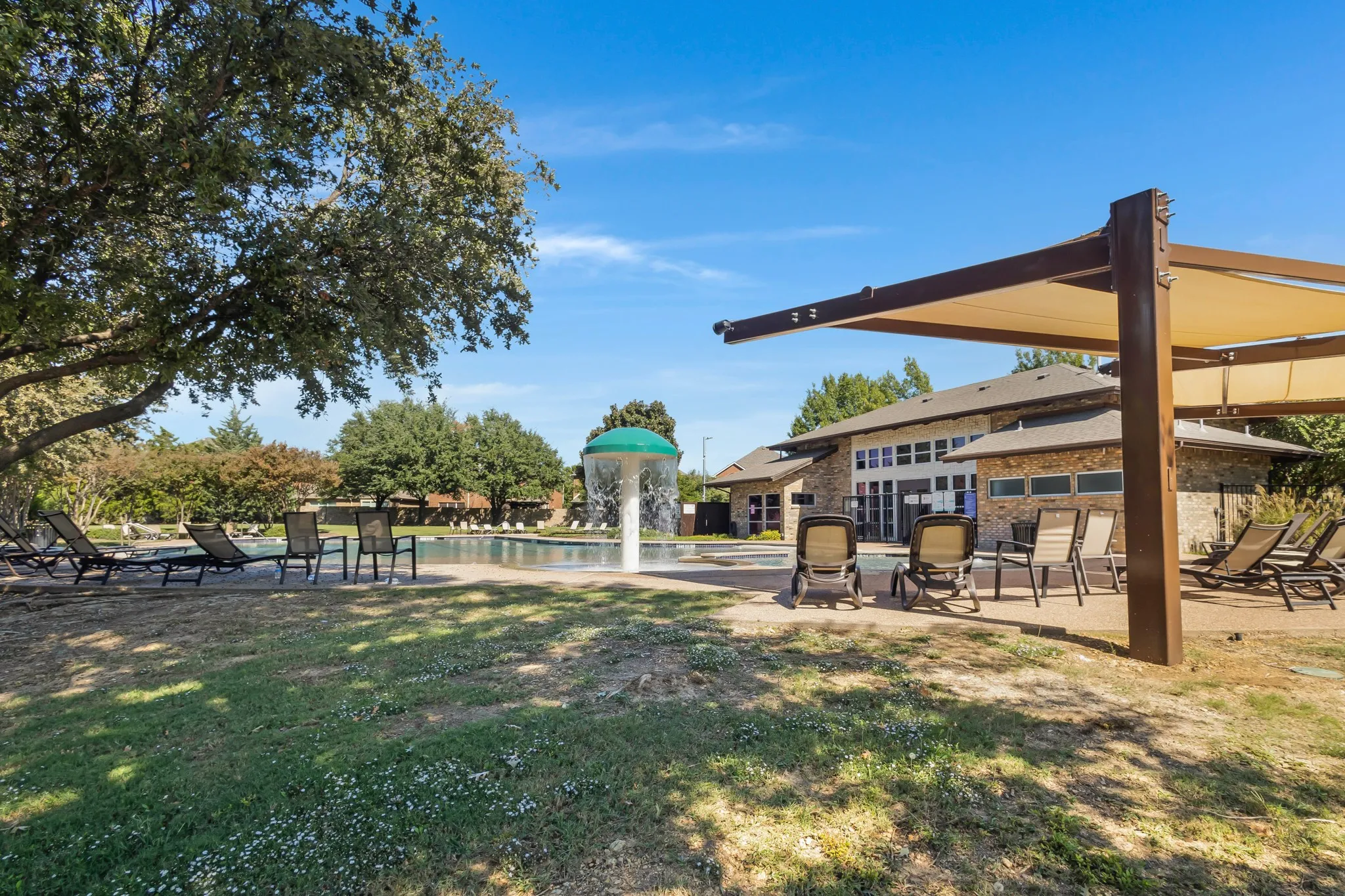 Outdoor pool area featuring a water feature, stone-clad building, and a shaded pergola