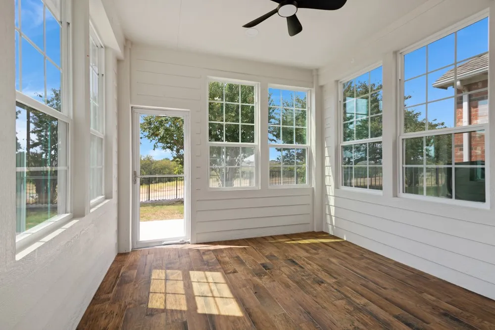 Enclosed sunroom featuring multiple windows, wood-finish flooring, white shiplap walls, a glass paneled door, and a ceiling fan