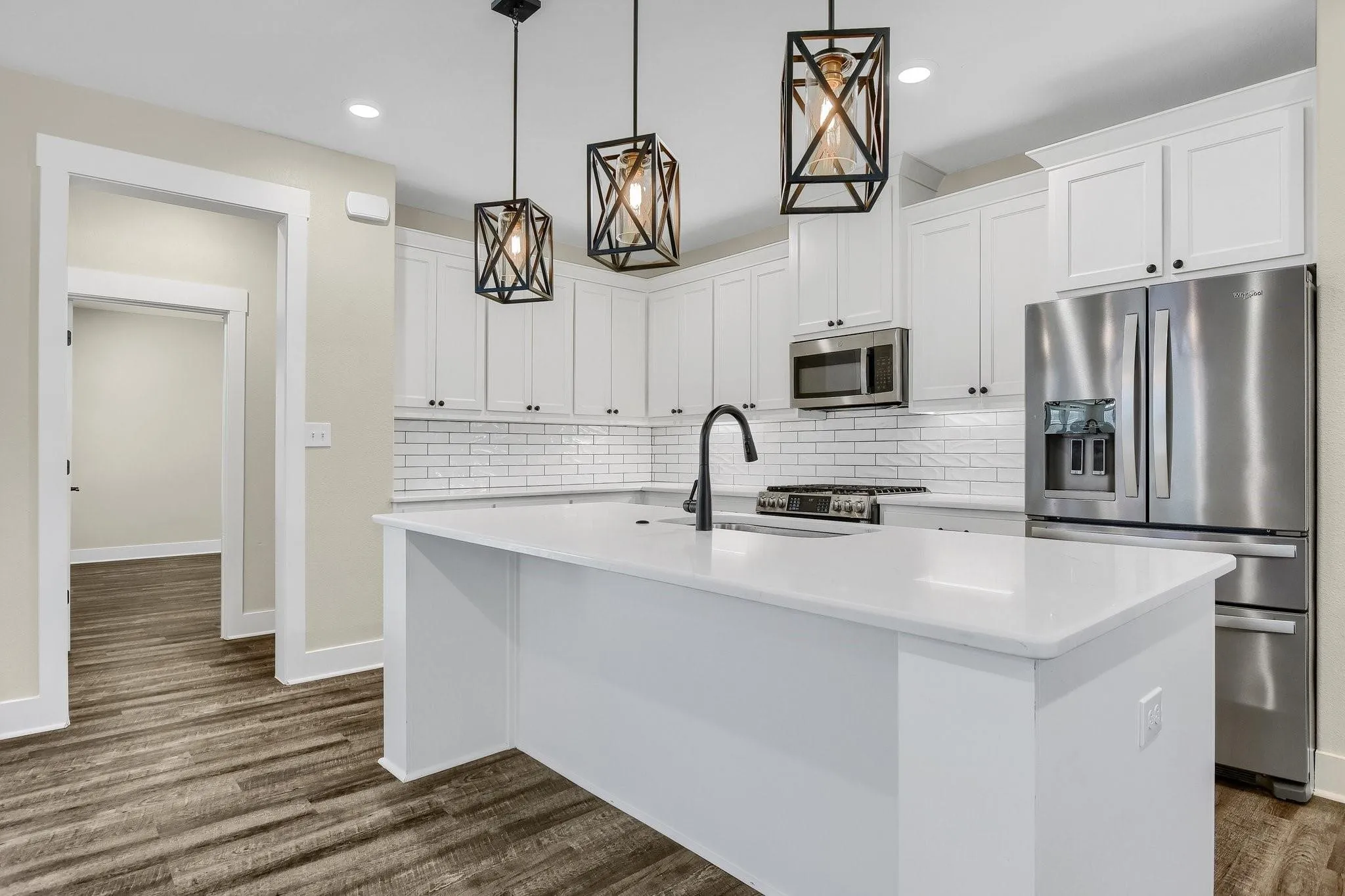 White kitchen island with a built-in sink, white cabinetry, stainless steel appliances, and wood-finish flooring