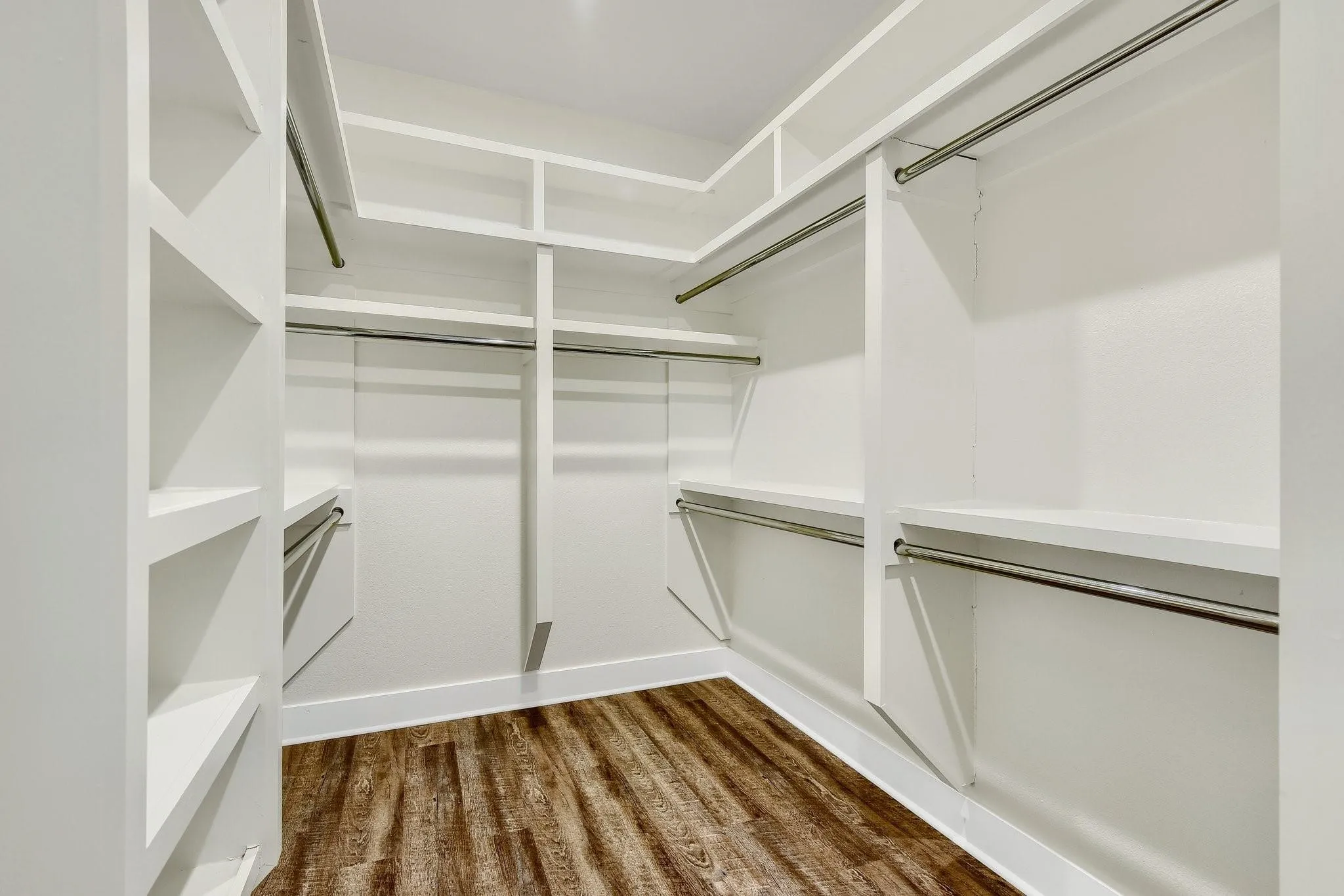 Spacious walk-in closet featuring custom white cabinetry with multiple shelving units, hanging rods, and brushed nickel hardware throughout