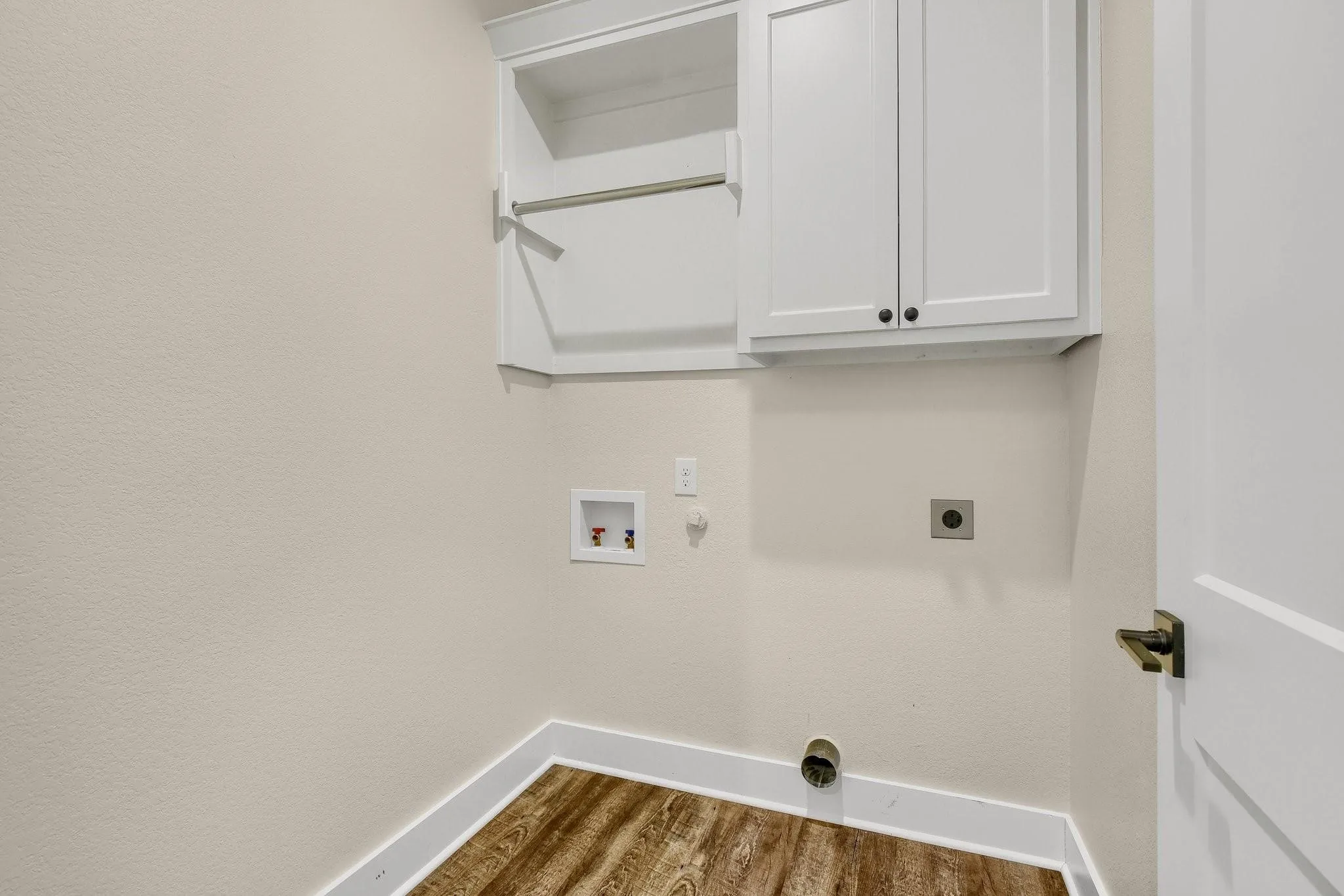 Laundry room with wood-finish flooring, white cabinetry with black hardware, and an integrated hanging rod