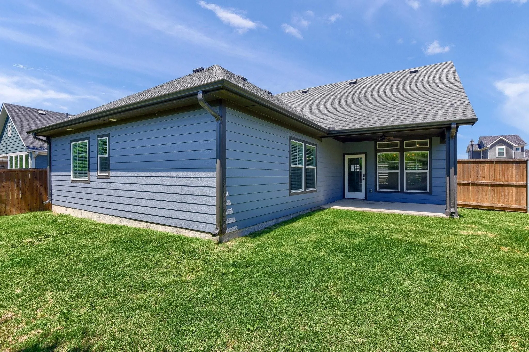 Expansive backyard with a covered patio, multiple windows, and a wood privacy fence