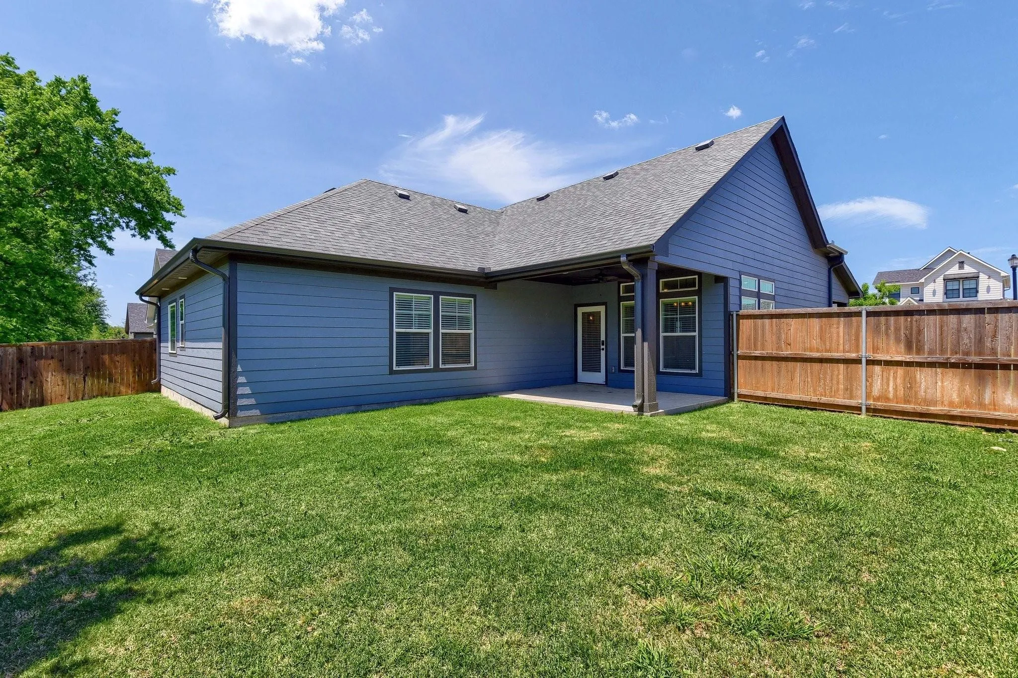 Expansive backyard featuring a manicured lawn, wood fencing, and a concrete patio