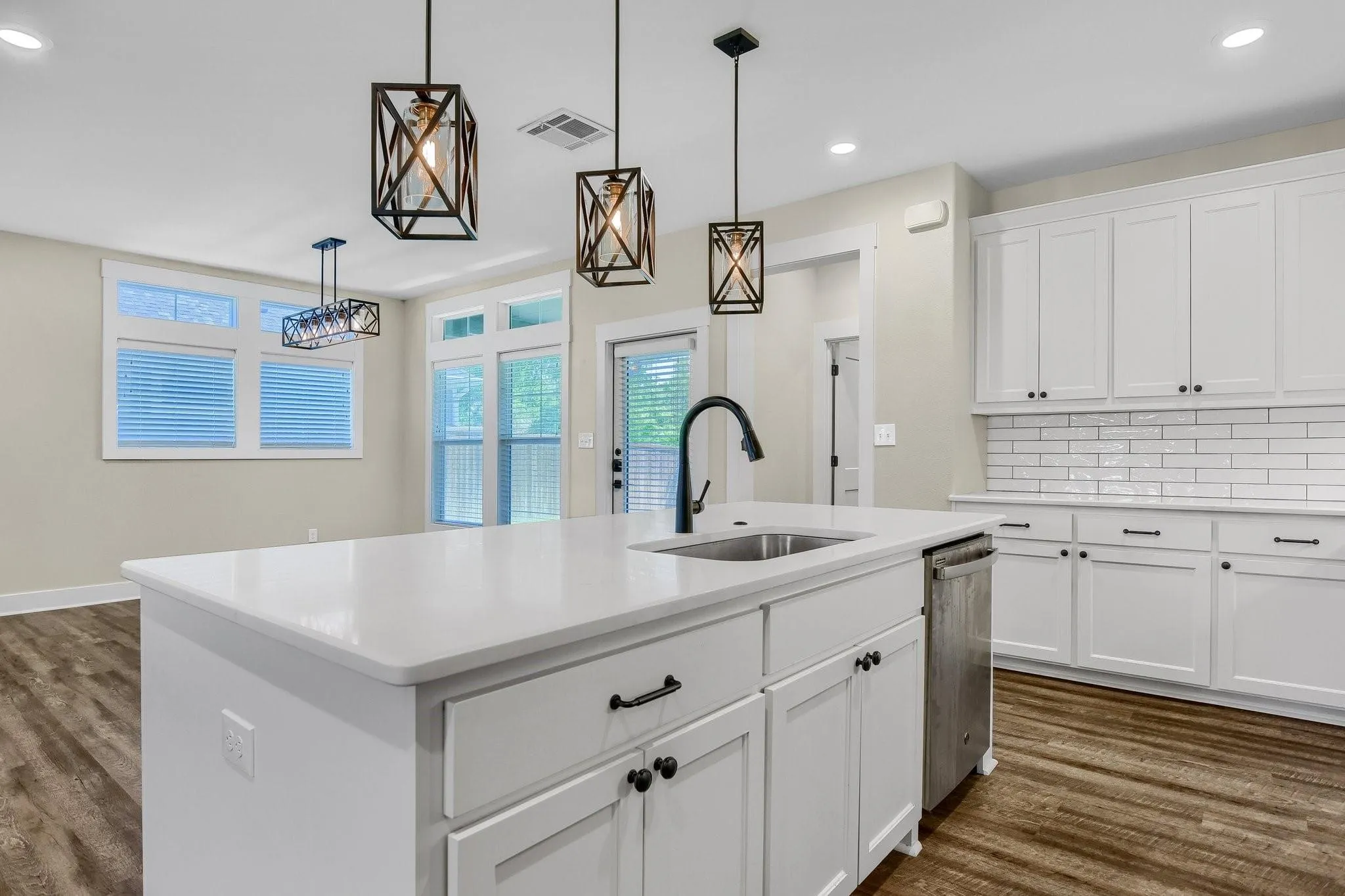 Kitchen featuring a center island with a built-in sink, white cabinetry with dark hardware, white subway tile backsplash, and wood-finish flooring