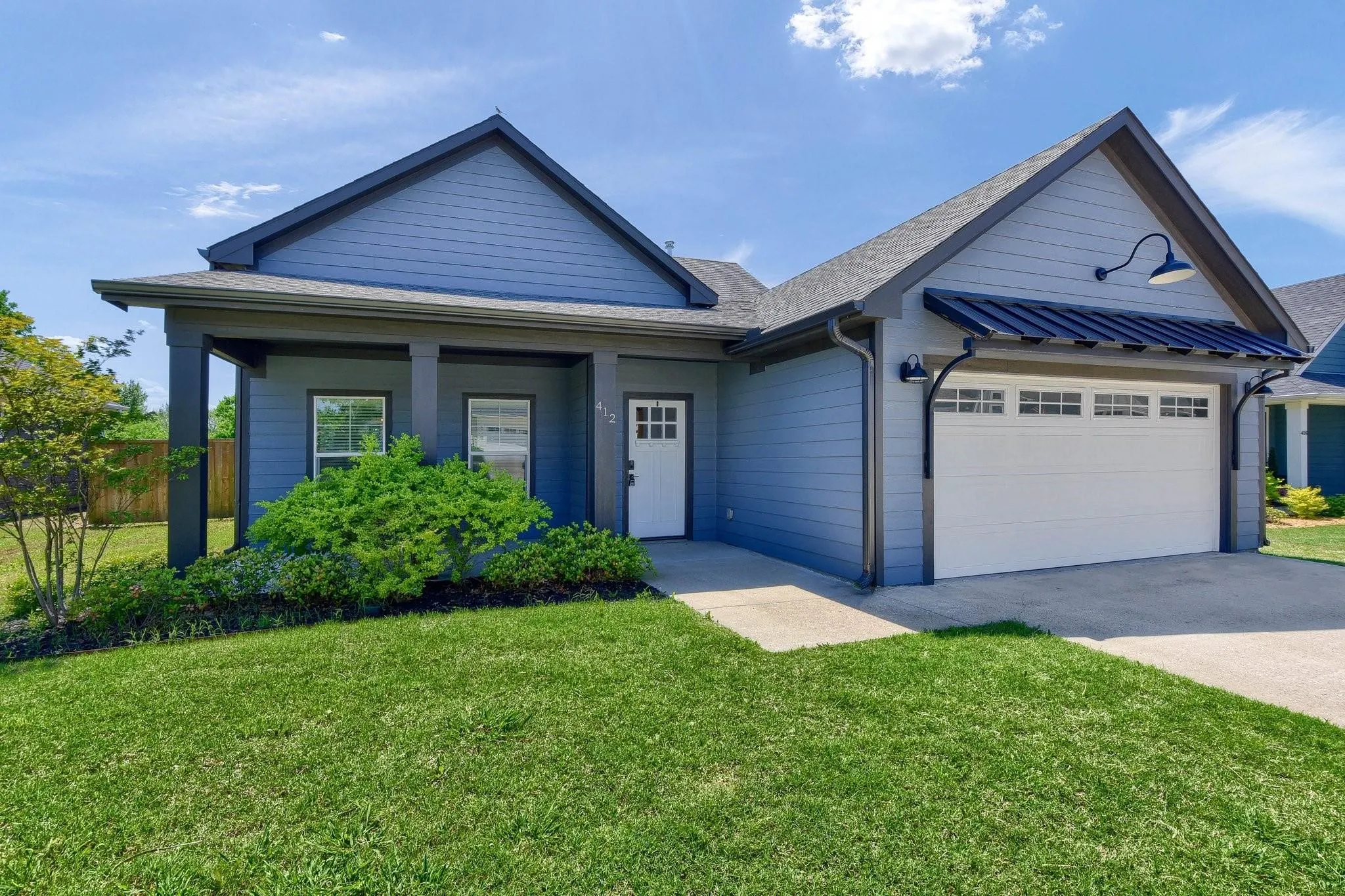 Modern exterior with blue siding, a covered entry, an attached garage with a dark metal awning, and a well-maintained lawn