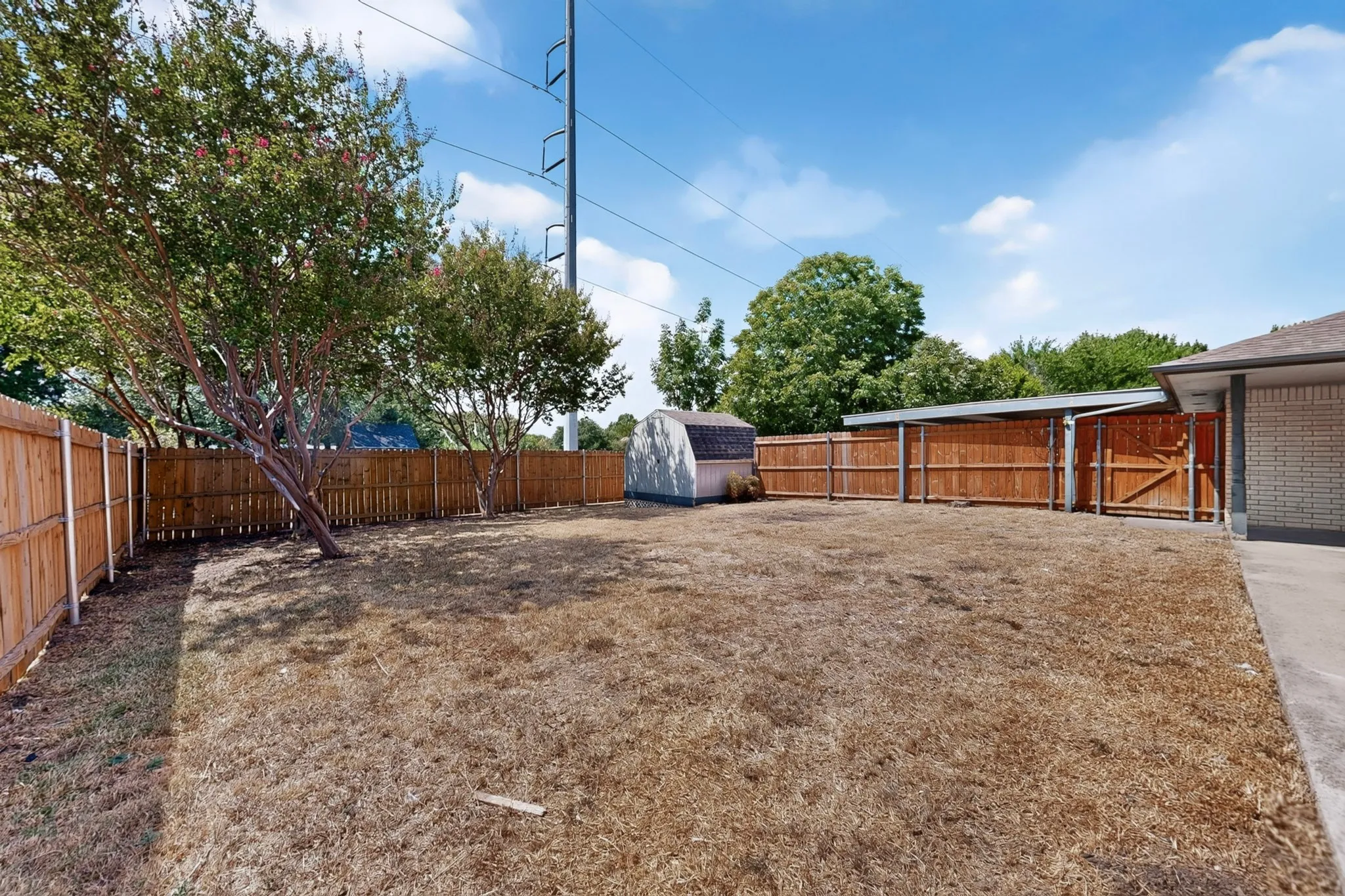 Fenced backyard with mature trees, a storage shed, and a covered patio area