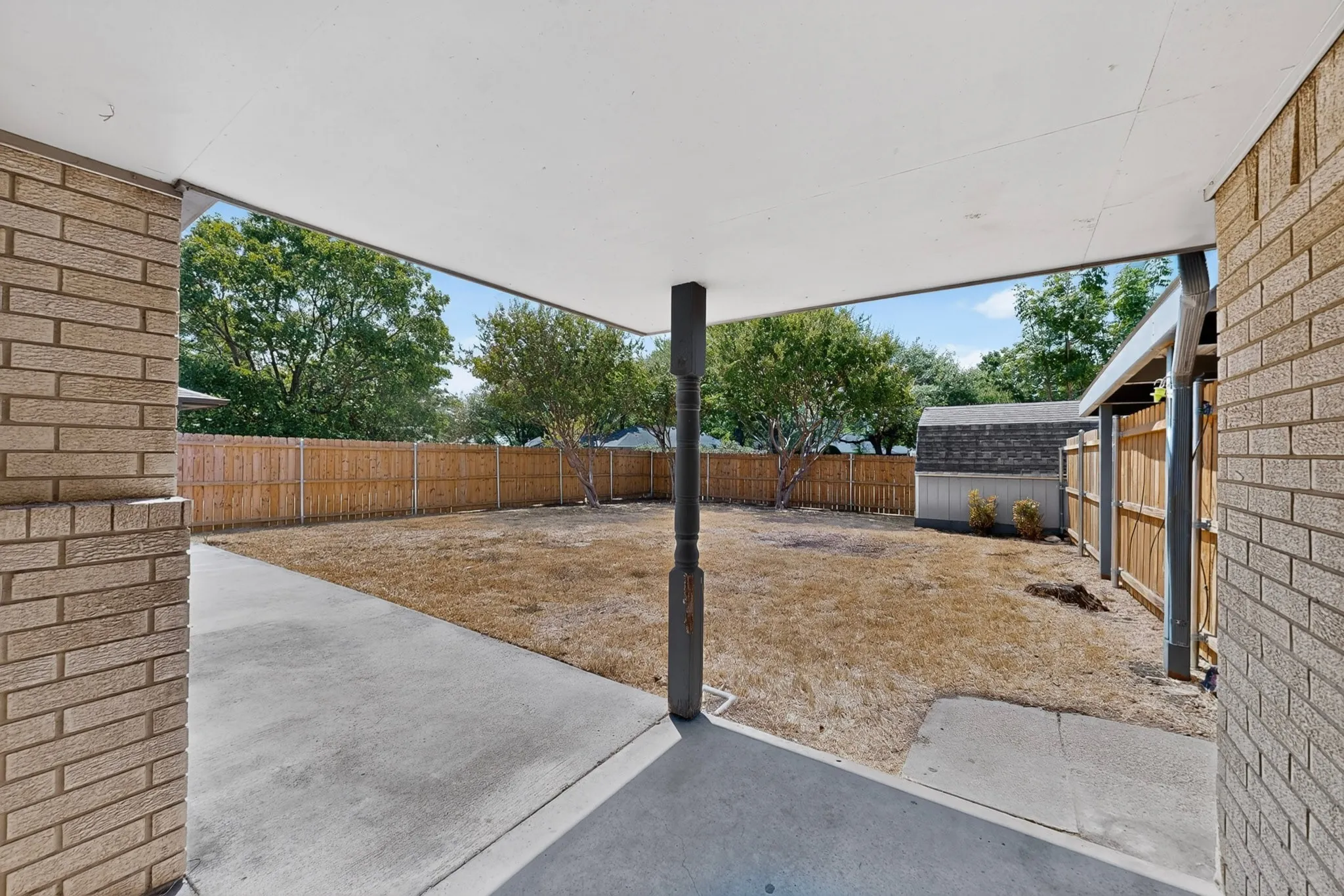 Covered patio with concrete flooring, brick exterior, and wood fencing