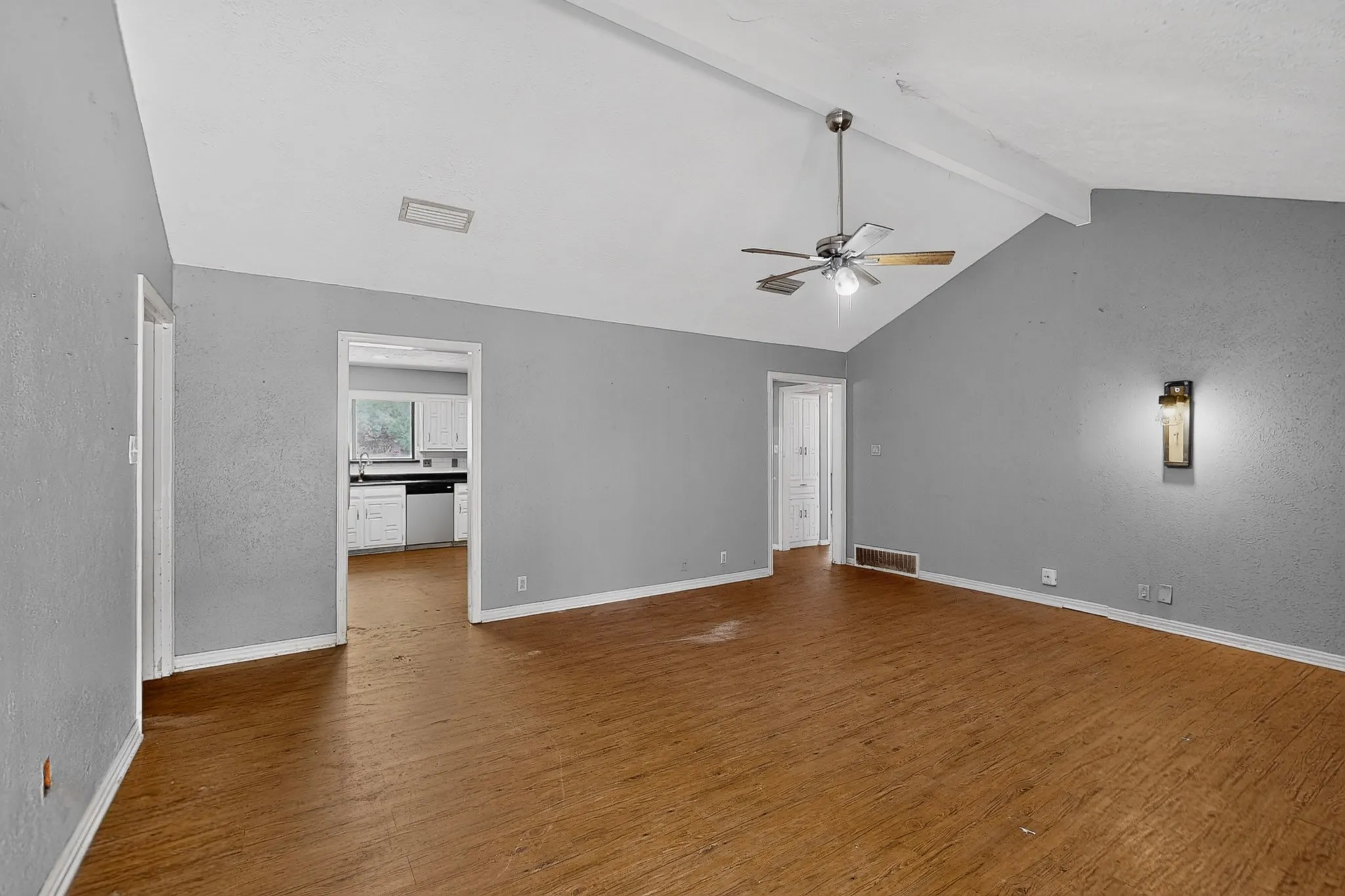 Vaulted ceiling with exposed beam, wood-finish flooring, and a ceiling fan