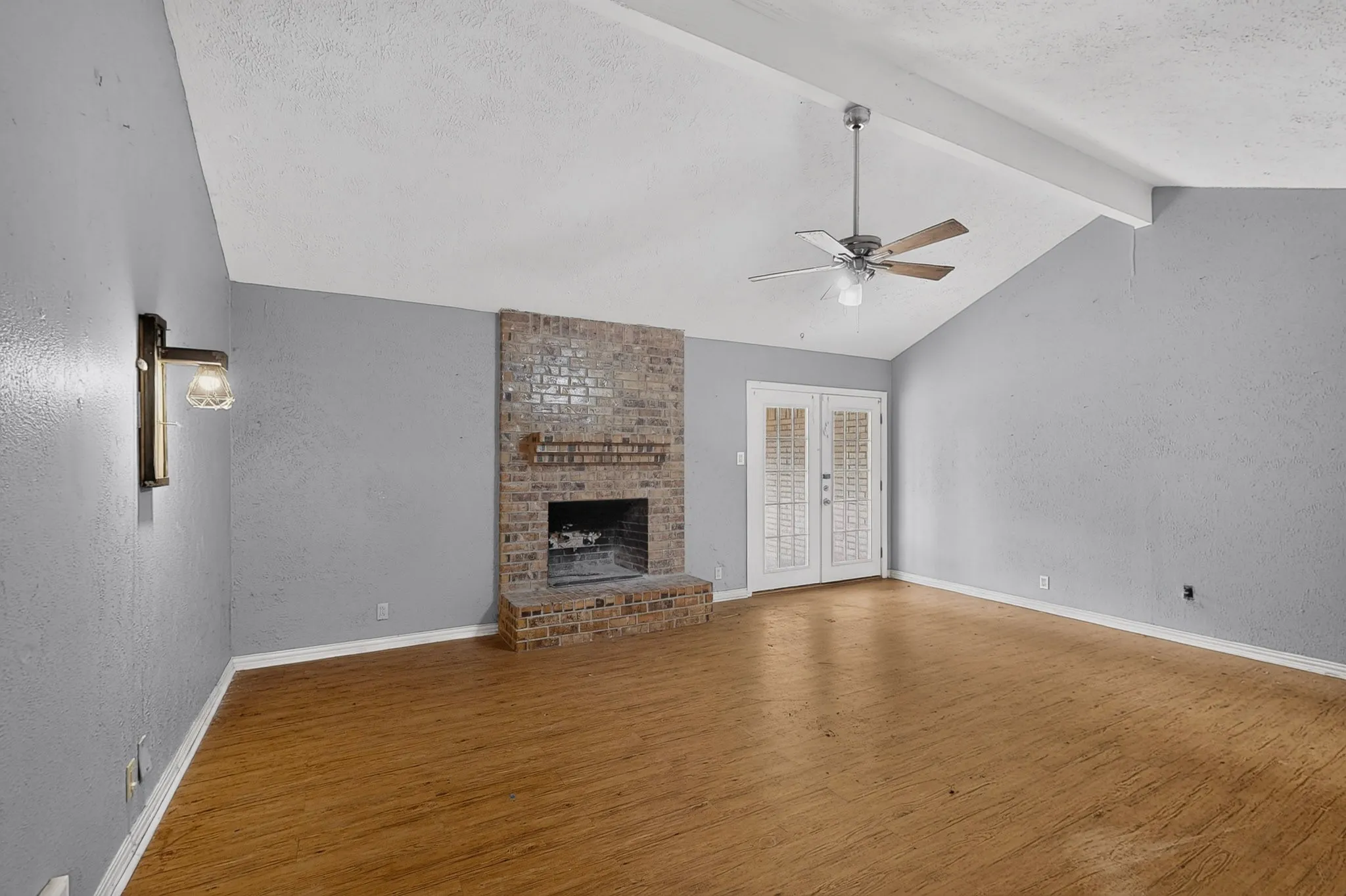 Vaulted ceiling with a ceiling fan, brick fireplace, wood-finish flooring, and French doors