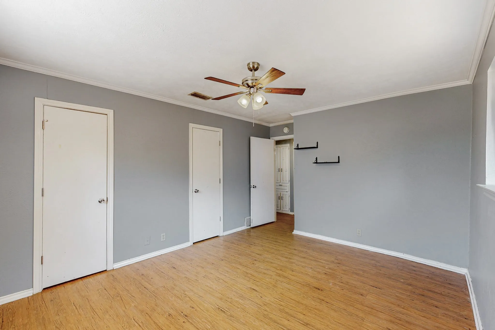 Wood-finish flooring, ceiling fan with integrated lighting, multiple white panel doors, and neutral wall tones