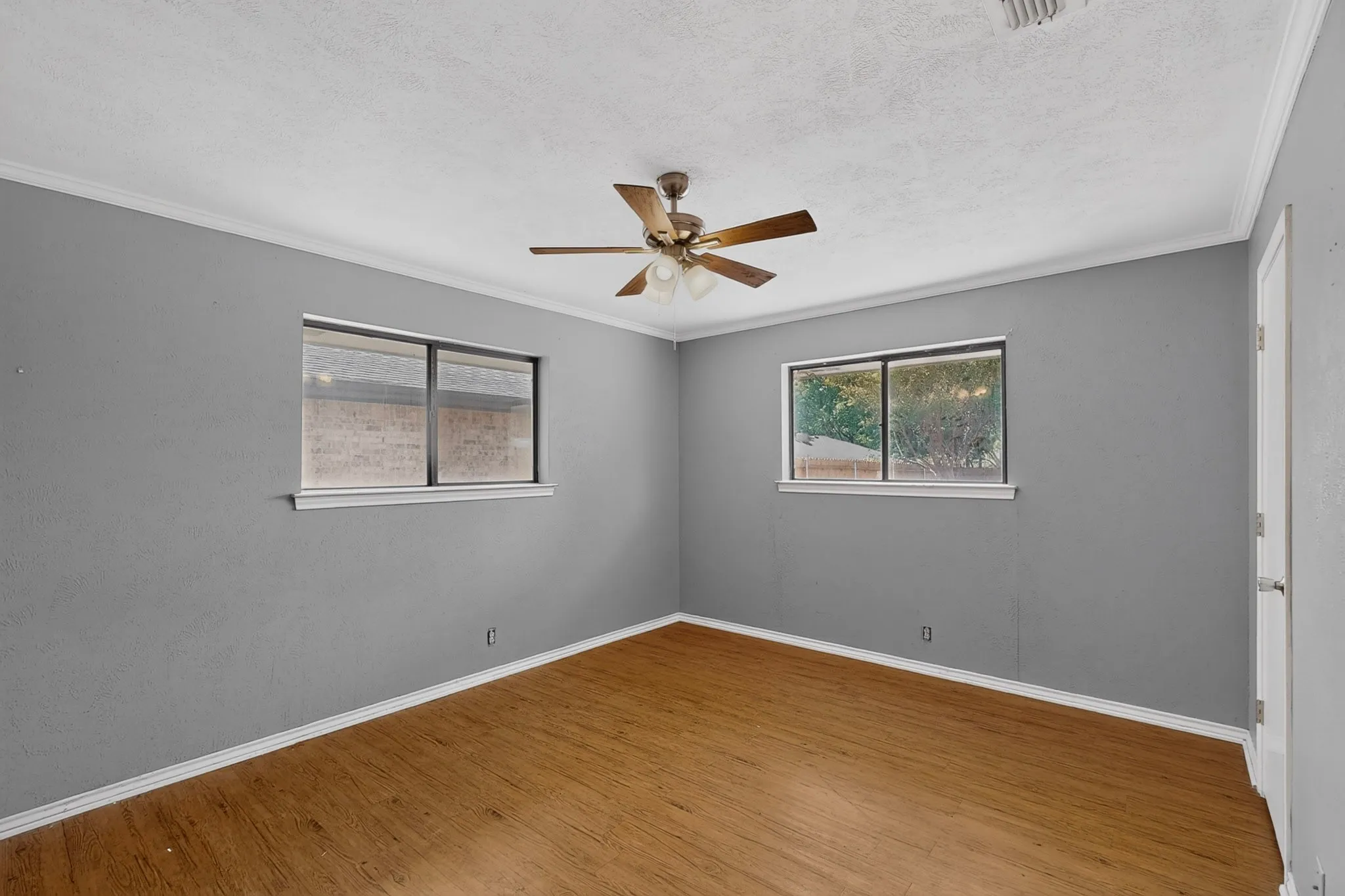 Wood-finish flooring, two windows, and a ceiling fan with light fixture