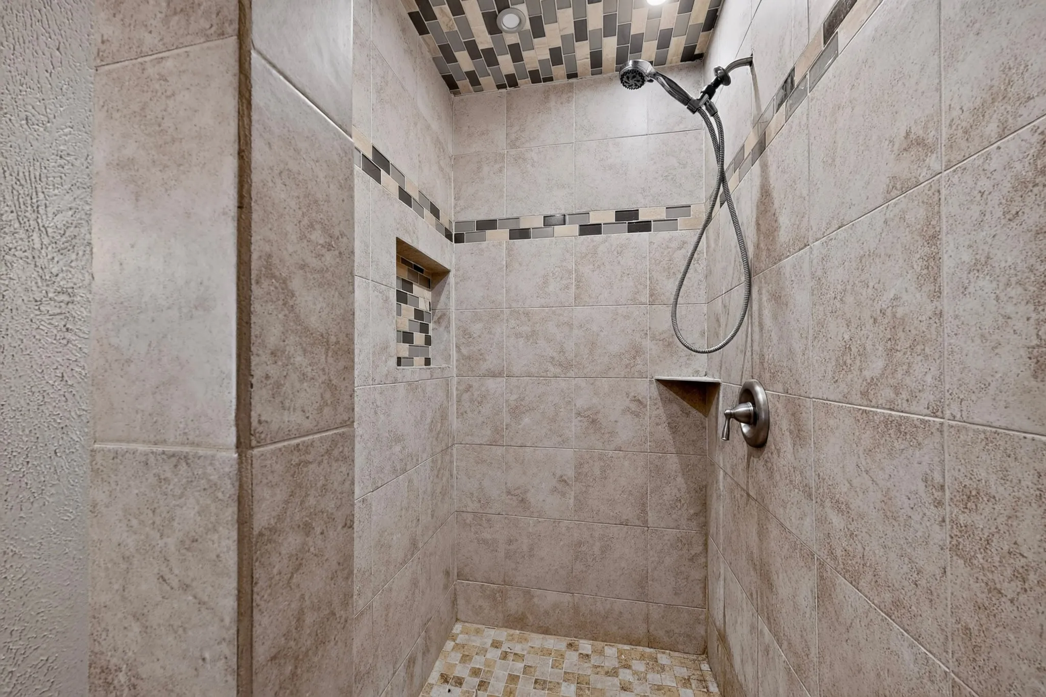 Tiled shower with handheld shower head, built-in shelving, and mosaic tile accents