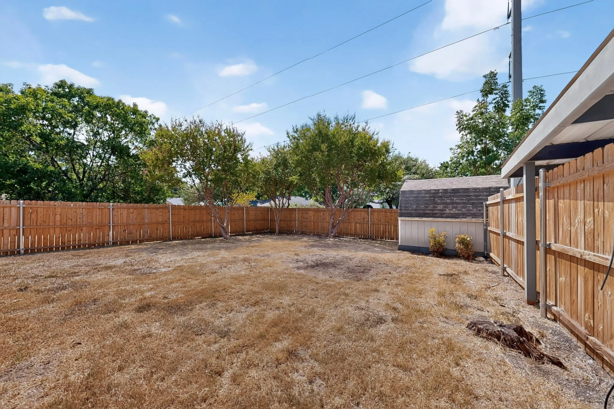 Fenced backyard with a storage shed and mature trees