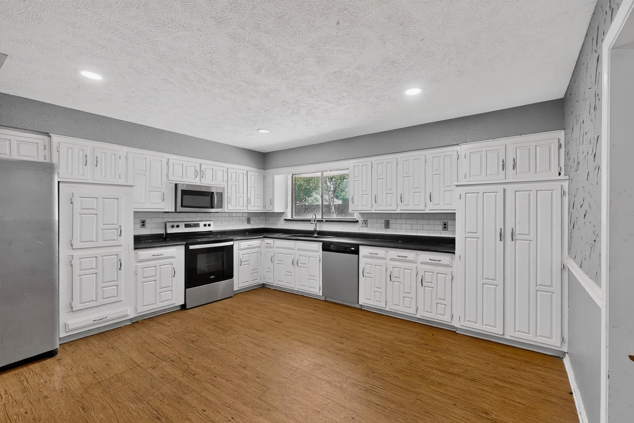 Kitchen featuring white cabinetry, wood-finish flooring, dark countertops, and stainless steel appliances