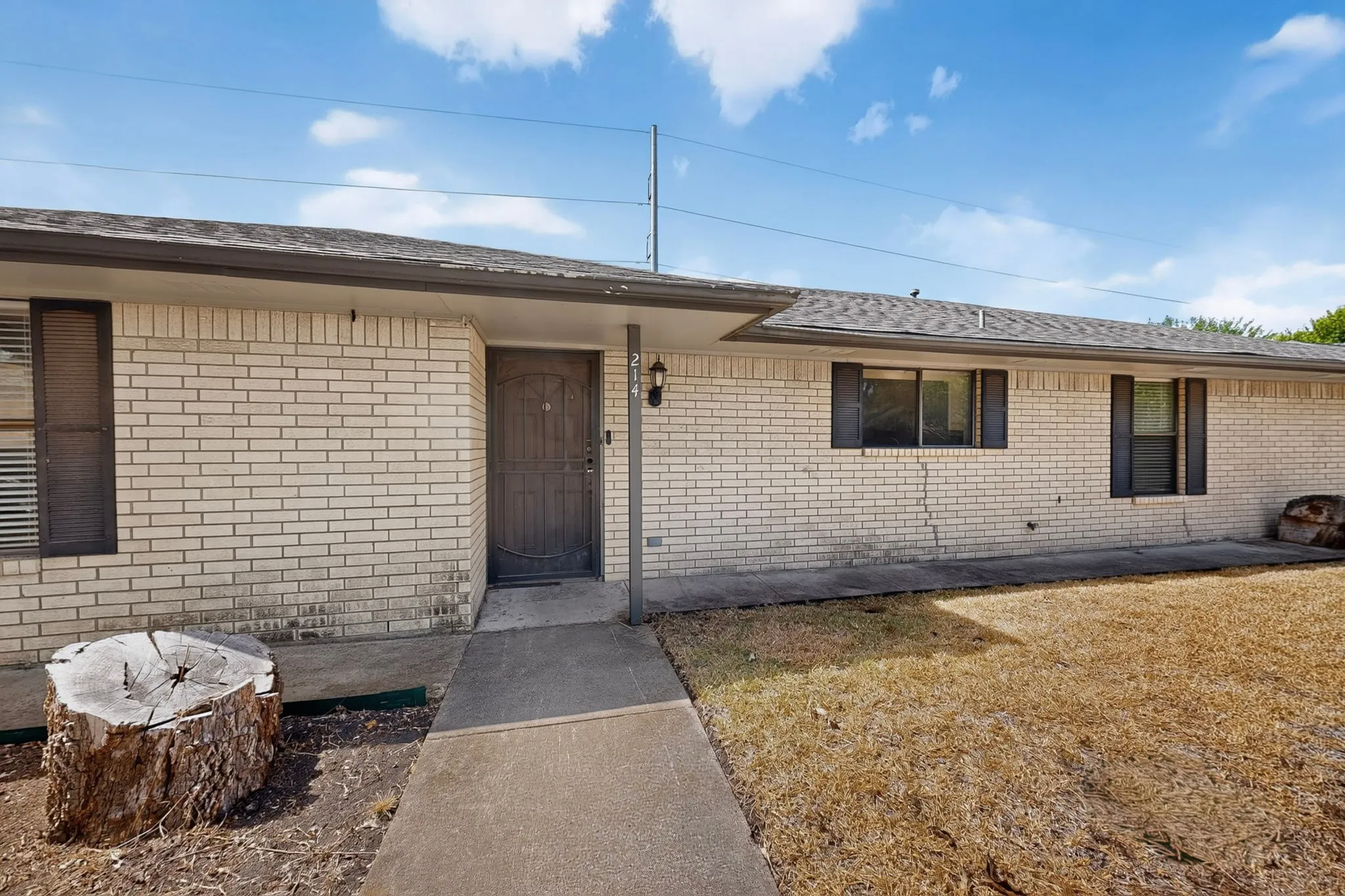 Brick exterior with a covered entry, dark-framed windows, and a concrete pathway