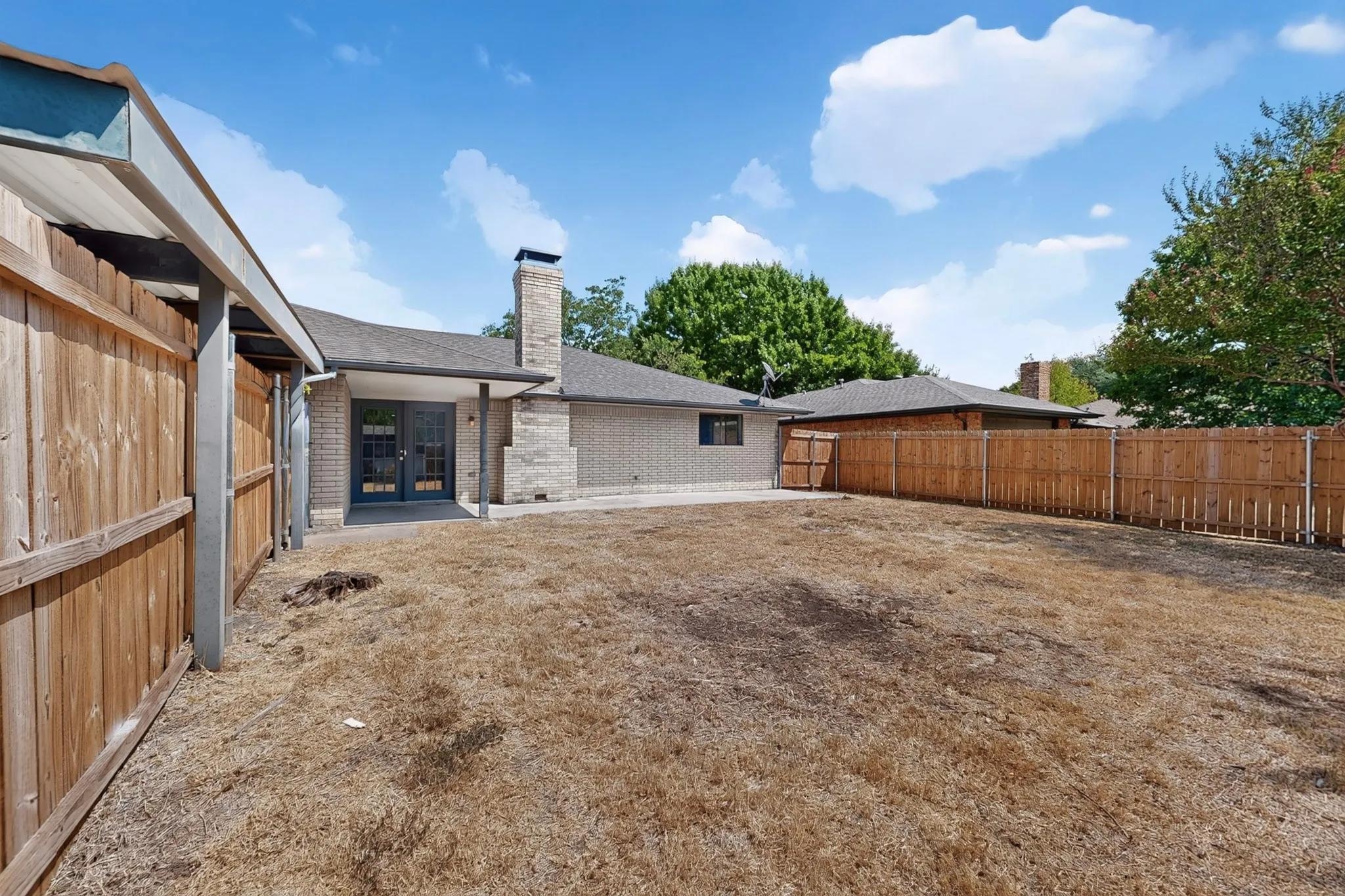 Expansive backyard featuring a wood privacy fence, brick exterior, and a covered patio with French doors