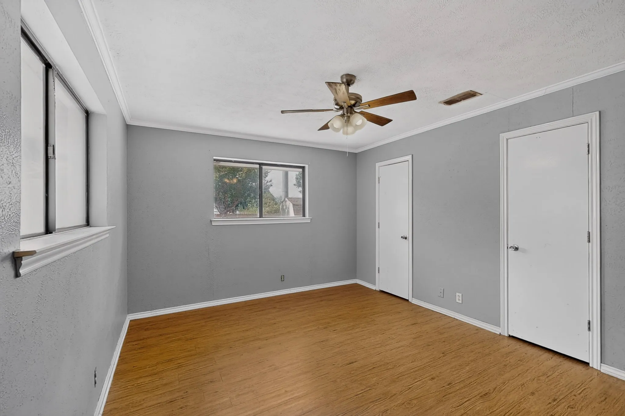 Wood-finish flooring, two windows, two white doors, ceiling fan with light fixture, and crown molding