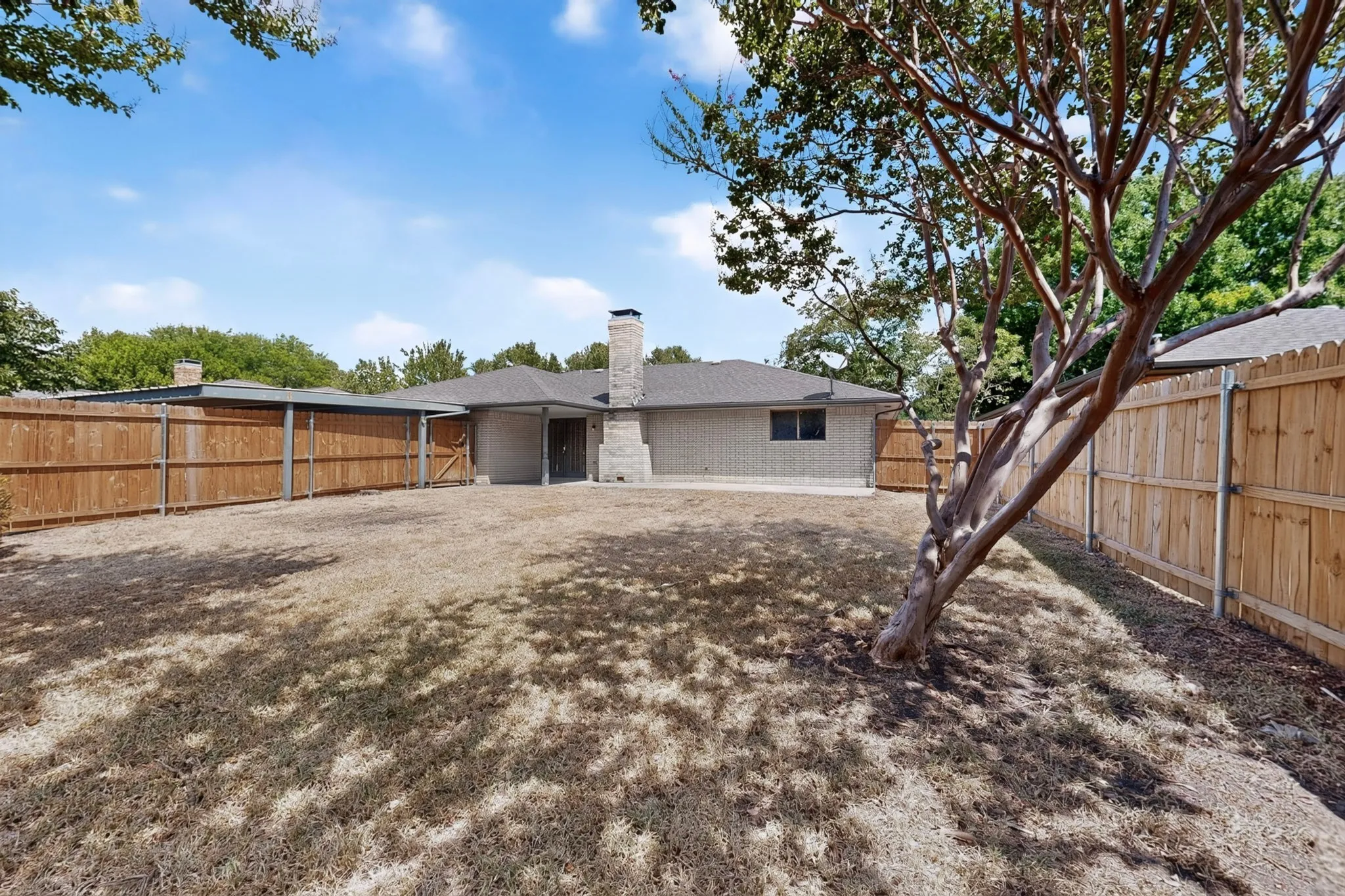 Expansive backyard featuring a privacy fence, covered patio, brick exterior, and a prominent chimney