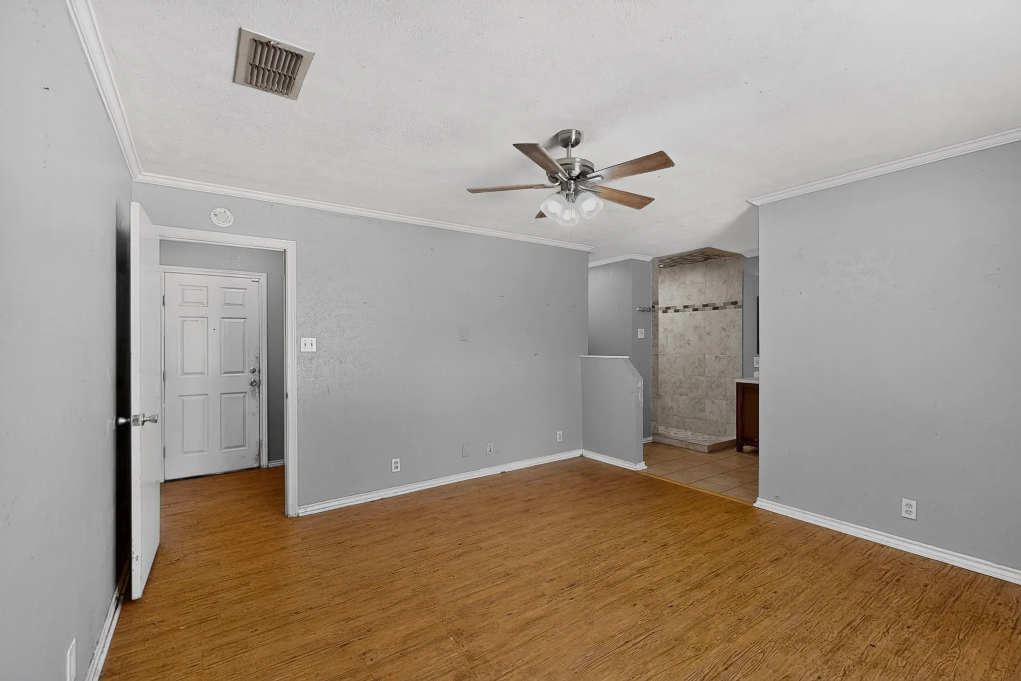 Wood-finish flooring throughout, ceiling fan with integrated lighting, crown molding, and a multi-panel interior door