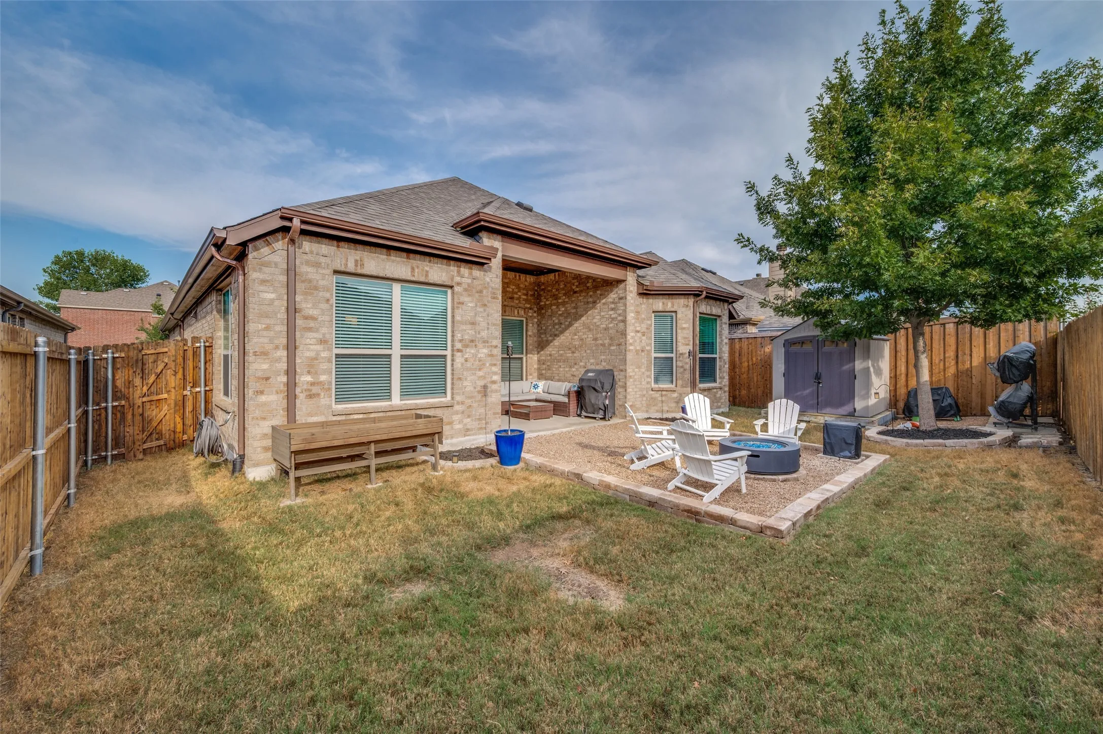 Brick exterior with a covered patio, a gravel patio with a fire pit, and a separate storage shed