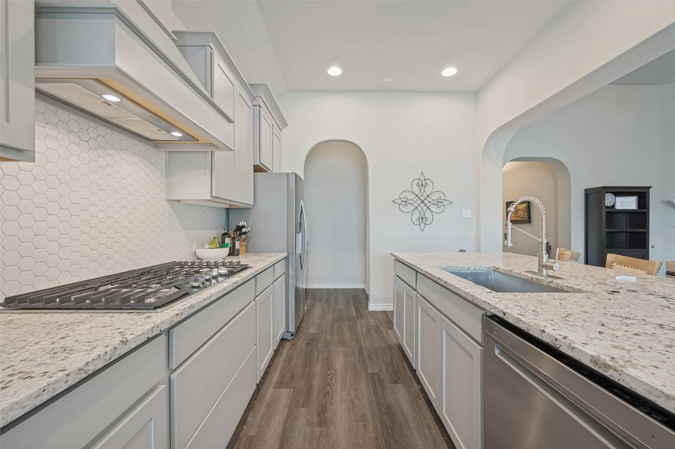 Kitchen featuring gray cabinetry, light speckled countertops, a hexagon tile backsplash, a gas range, and wood-finish flooring