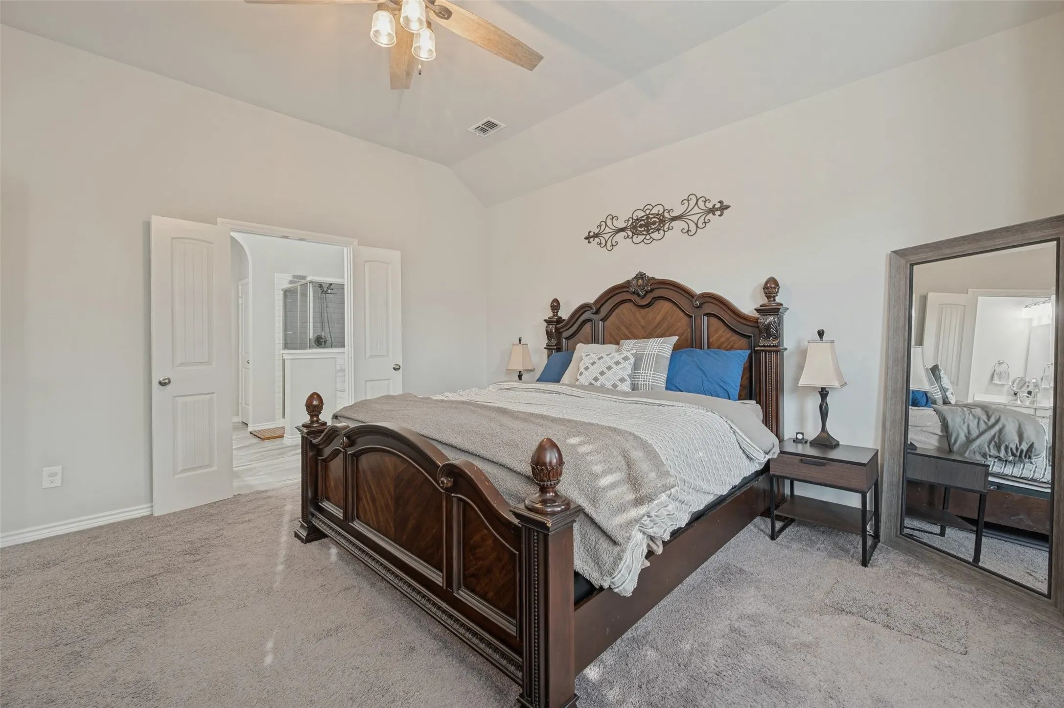 Carpeted room featuring a vaulted ceiling with a ceiling fan, double panel doors, and a partial view of a bathroom with a shower enclosure