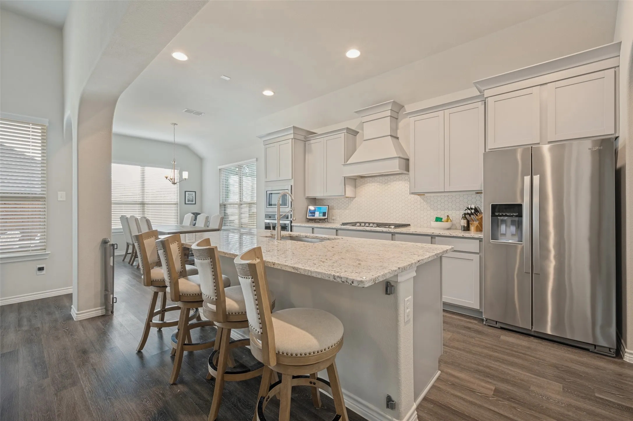 Open-concept kitchen featuring an island with Granite Countertops, stainless steel appliances, light-toned cabinetry, and wood-finish flooring