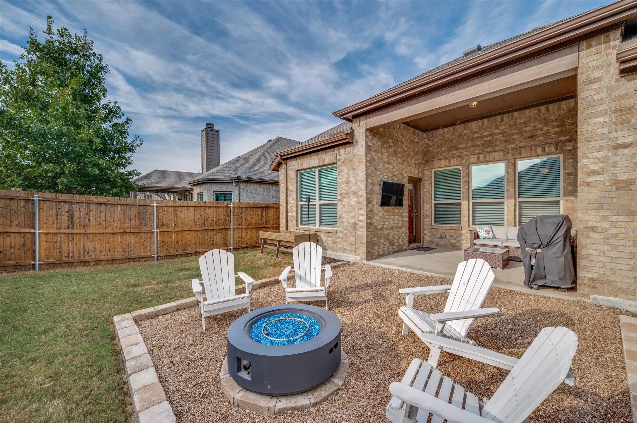 Expansive backyard featuring a stone-edged gravel patio with a built-in fire pit, a covered outdoor living area, a privacy fence, and a manicured lawn