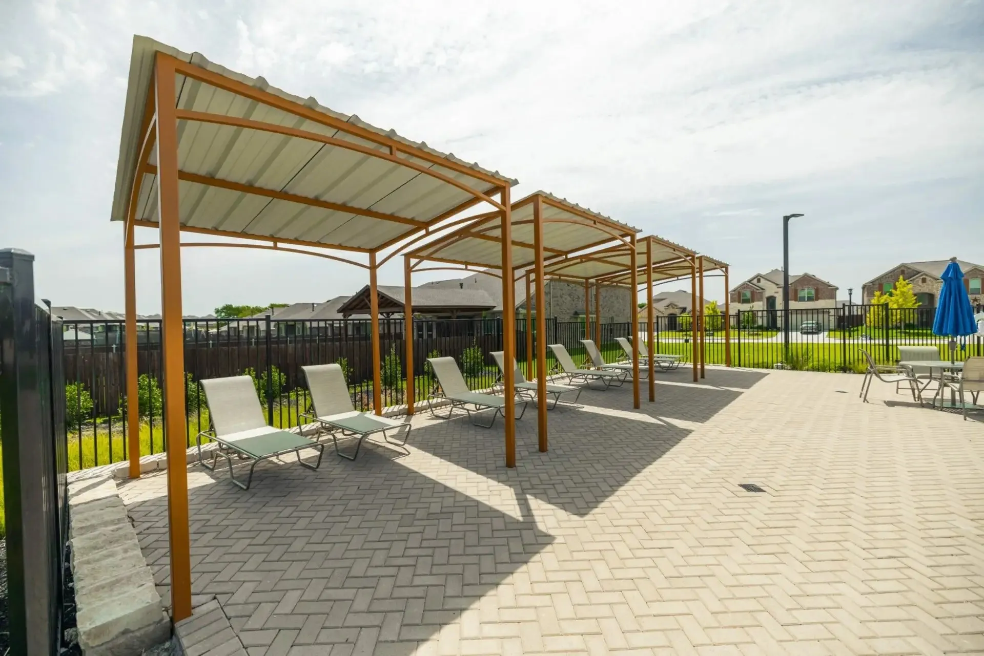 Shaded lounging area with multiple canopies, a paver patio, and a metal fence