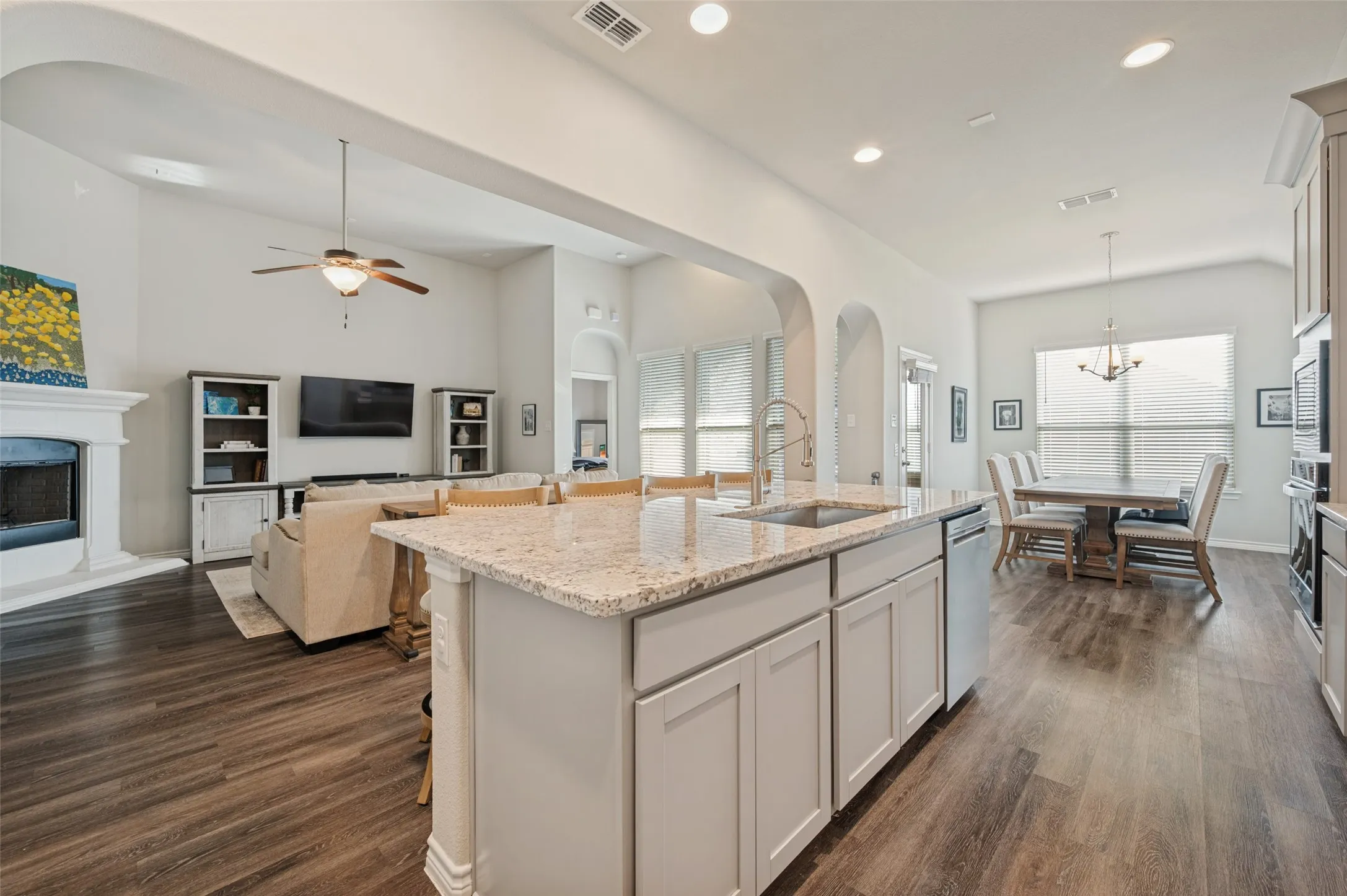 Open-concept living area with wood-finish flooring, a kitchen island with integrated sink, recessed lighting, and a dining area with chandelier