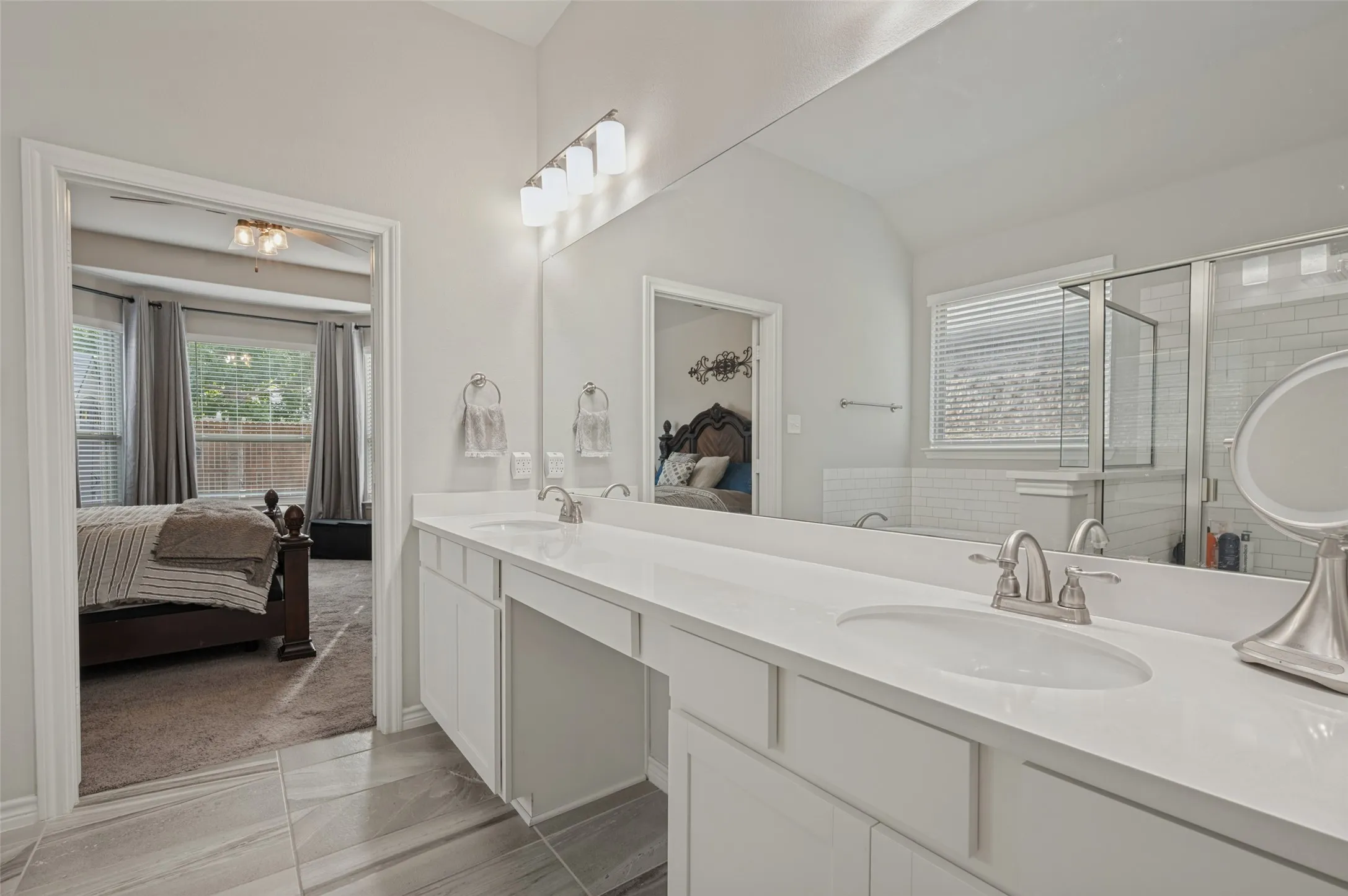 Dual vanity with white cabinetry and integrated sinks, brushed nickel fixtures, a large wall-mounted mirror, and tile flooring