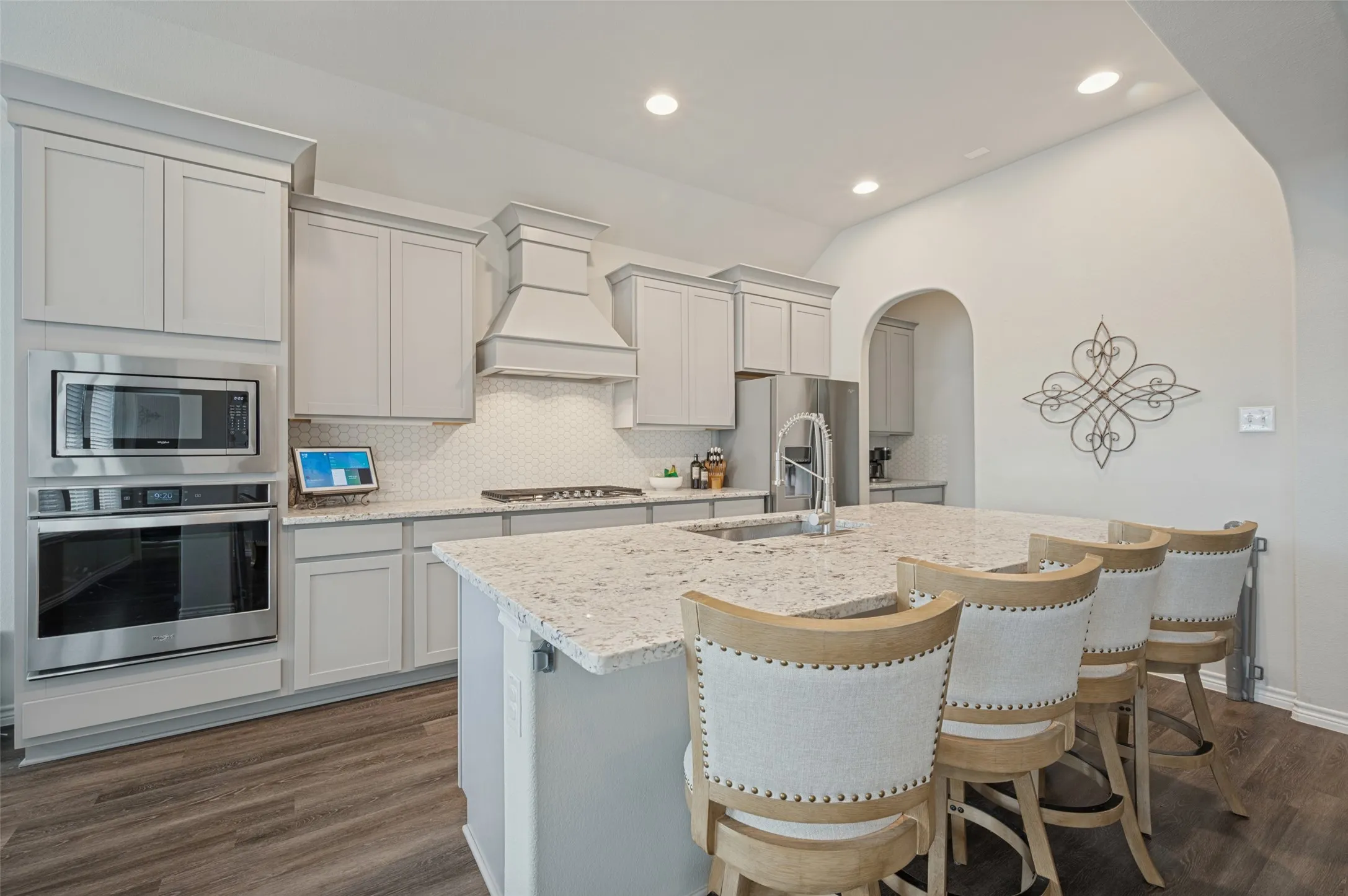 Kitchen featuring light gray cabinetry, stainless steel appliances, a center island with light-toned stone countertops, a hexagonal tile backsplash, and wood-finish flooring