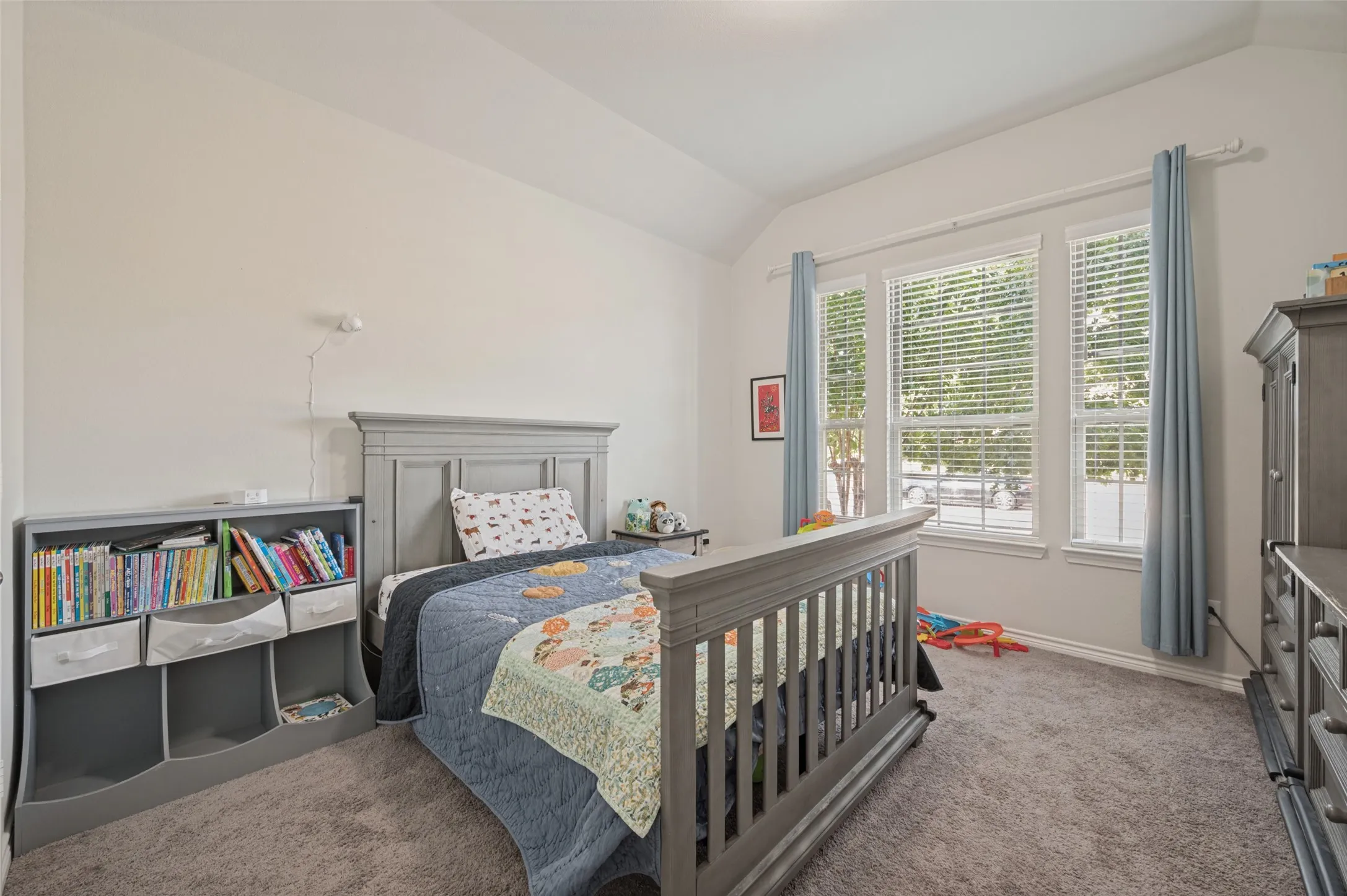 Vaulted ceiling, triple windows with blinds, light wall color, and grey carpet flooring