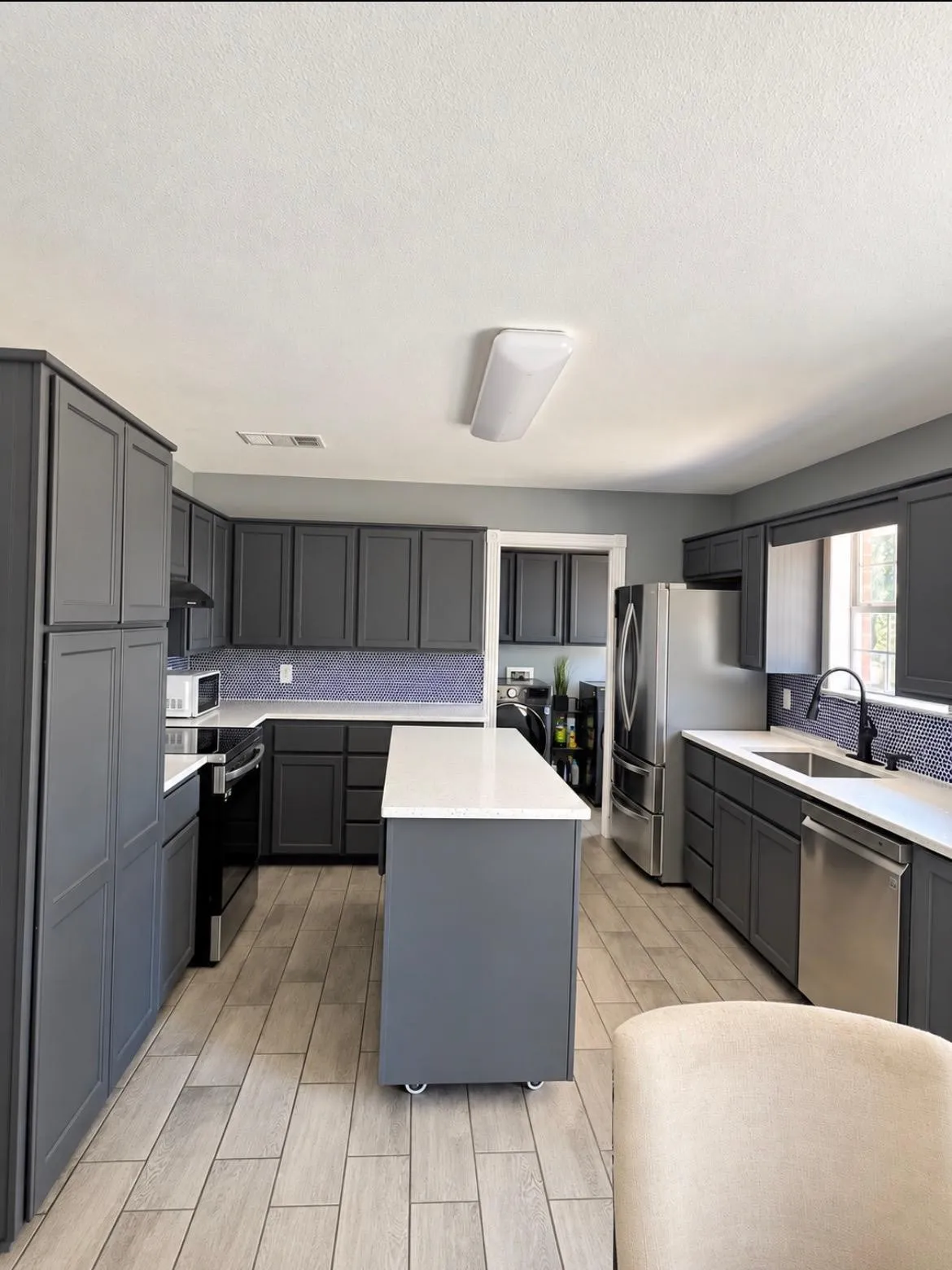 Kitchen featuring wood-finish flooring, dark cabinetry, light countertops, and a mosaic tile backsplash