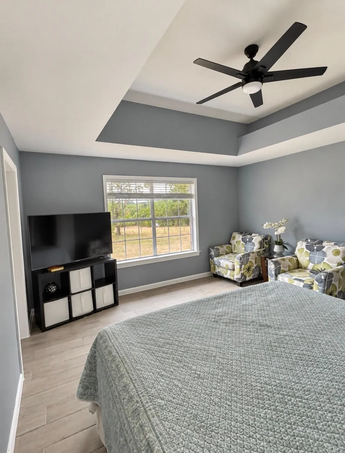 Tray ceiling with a ceiling fan, light-toned tile flooring, and a large window