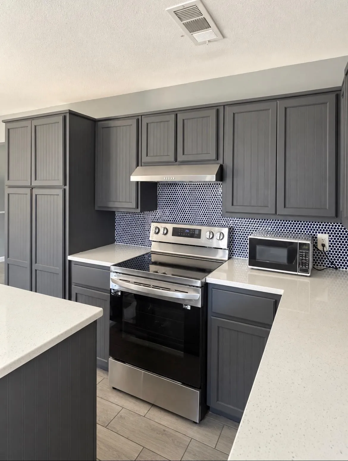 Kitchen featuring gray cabinetry, light-toned countertops, a blue penny tile backsplash, stainless steel appliances, and wood-finish flooring