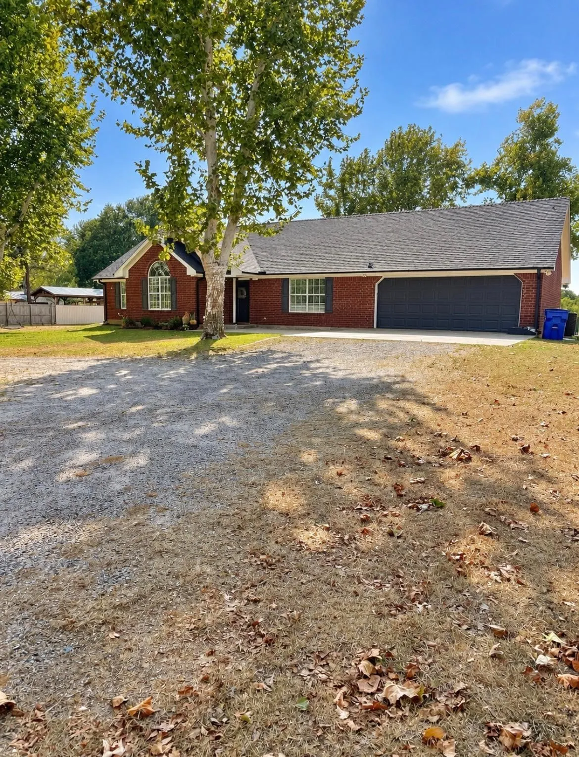 Brick exterior with an arched window, a two-car garage, and a gravel driveway